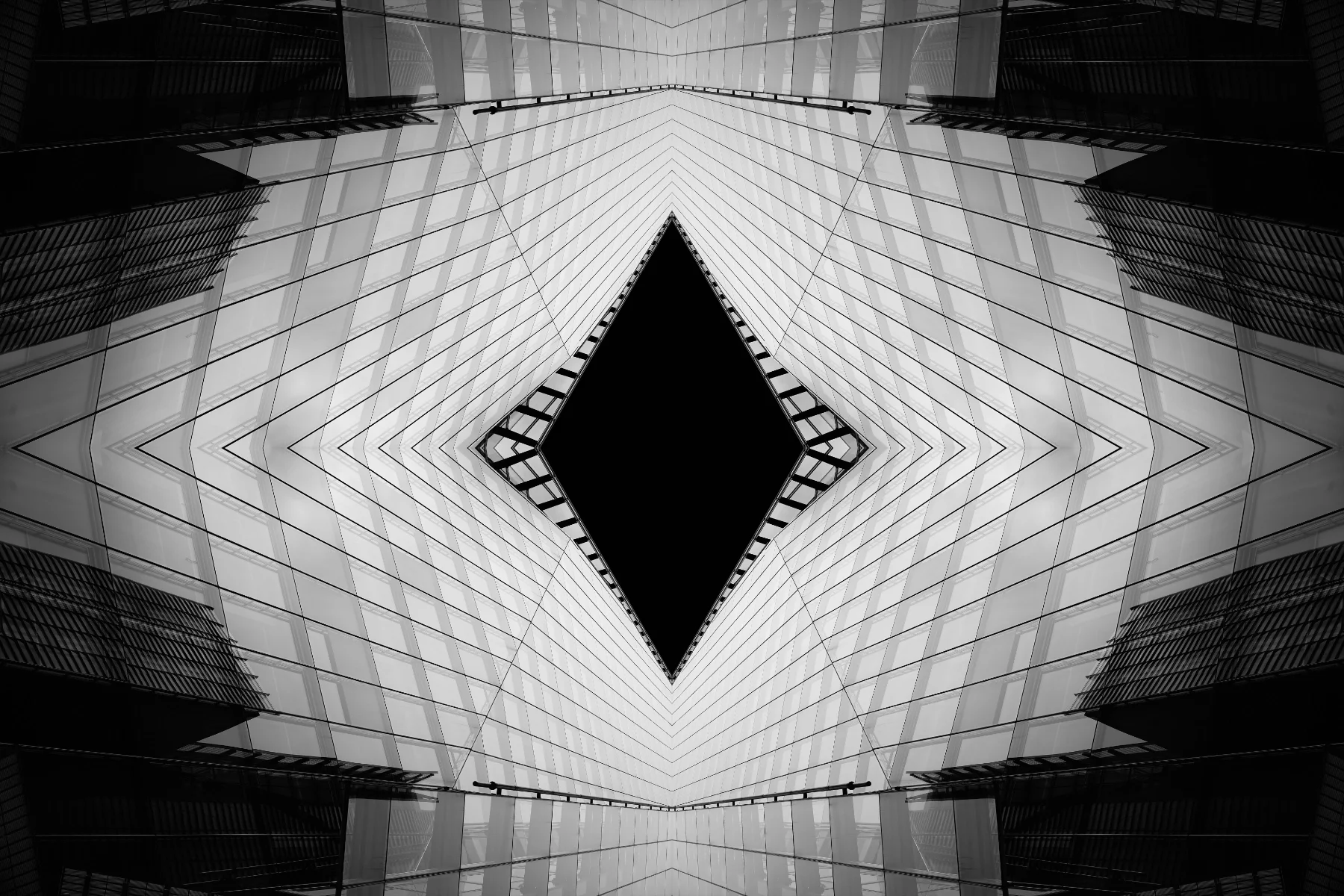 Symmetrical view of a modern, glass-covered skyscraper with a black, empty diamond-shaped space in the center, taken from below looking upward.