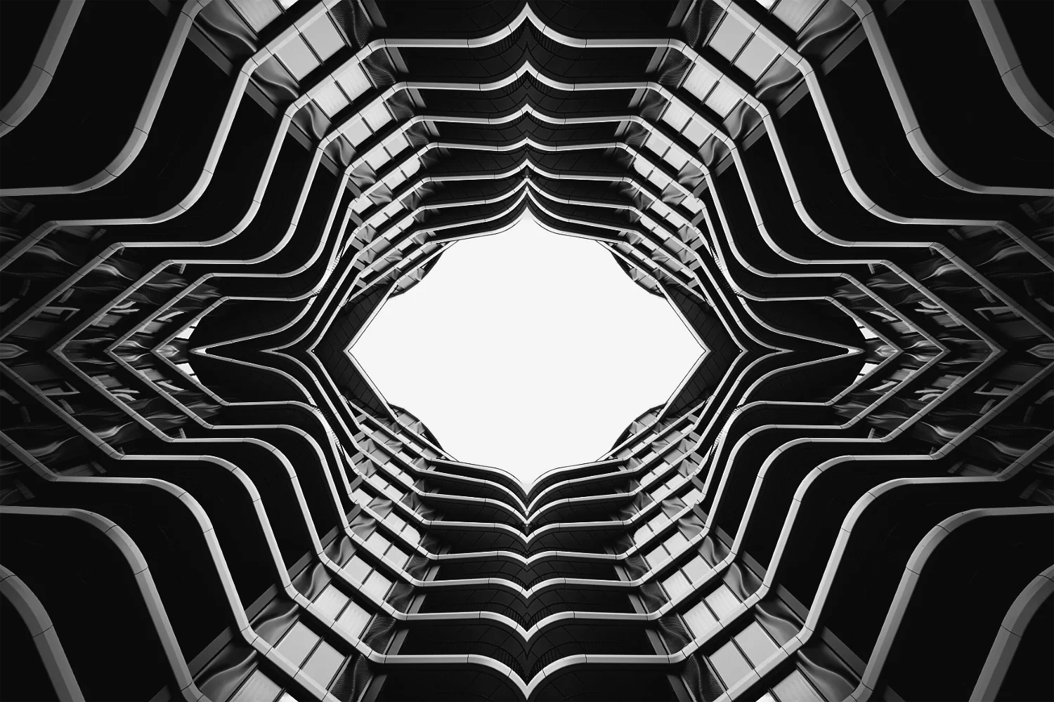 Looking up at the center of a tall, modern building with multiple balconies forming a geometric pattern around a bright, white sky.