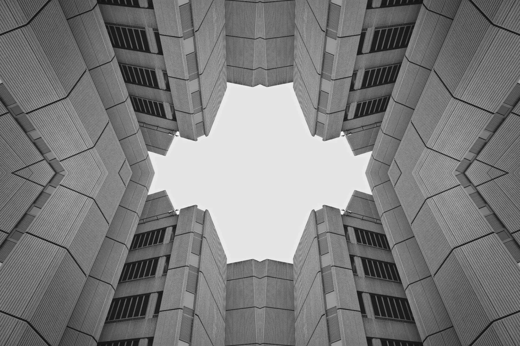 A black and white photo taken from below of the exterior of a modern building, looking up at a central opening in the structure.