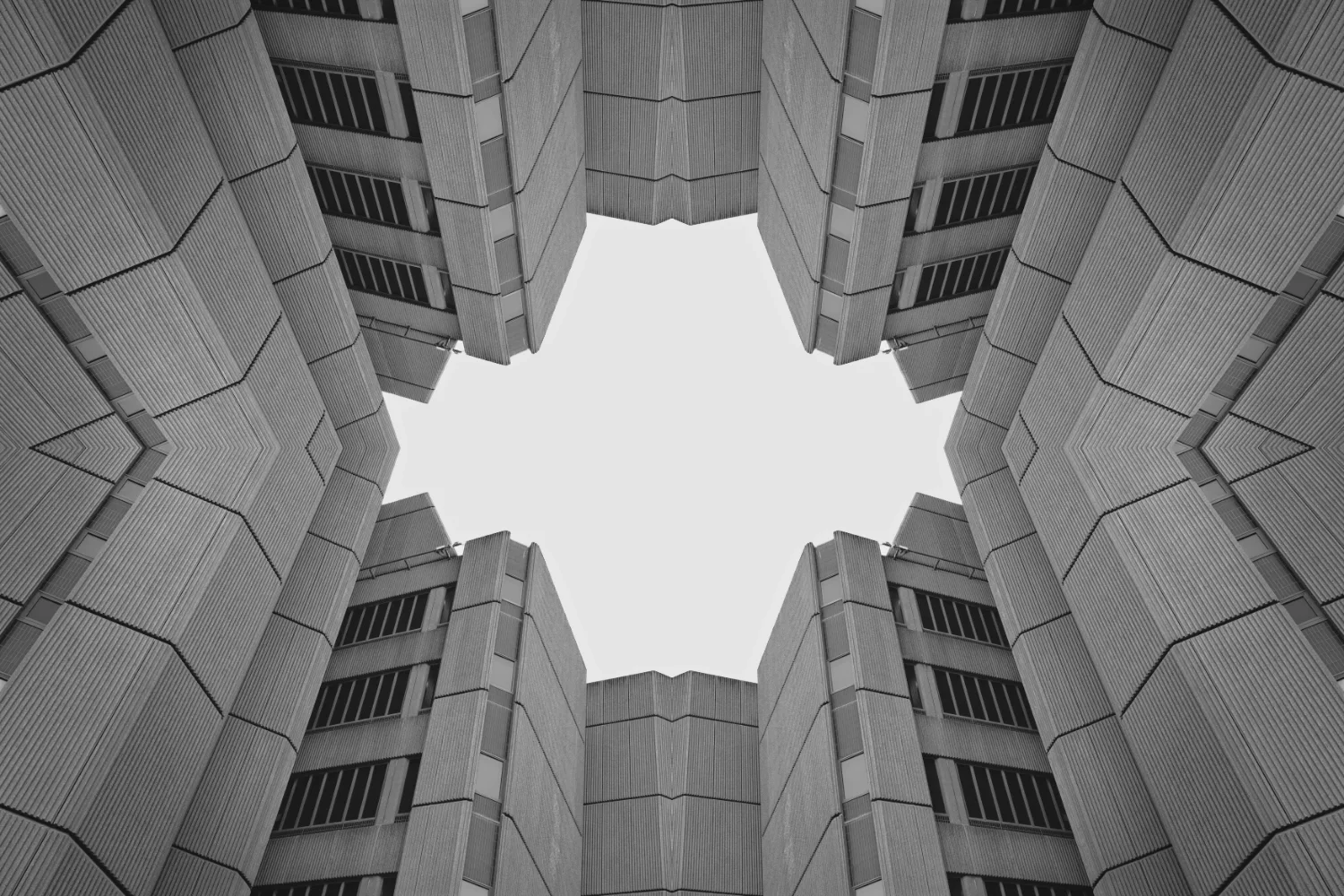 Looking upward at a modern multi-story building exterior with a hexagonal sky opening in the center, black and white