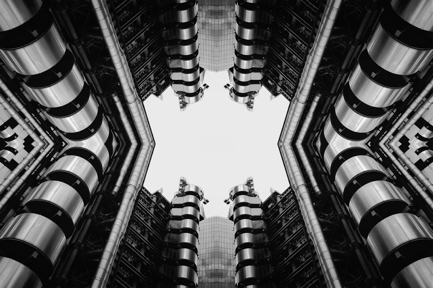 Looking up at a modern office building with multiple stories, curved metallic balconies, and pipes along the exterior, forming a square frame in the sky.