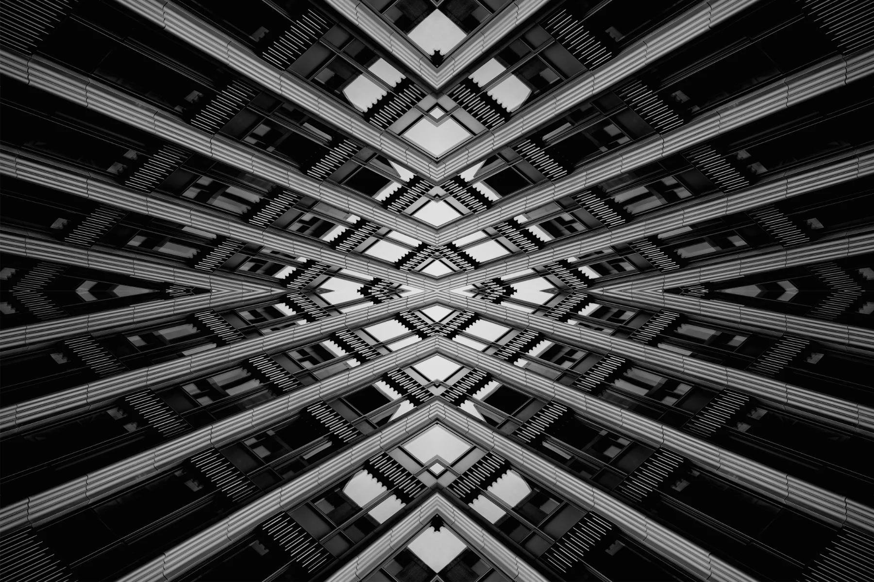 A mirrored, symmetrical view of a modern building's facade with glass windows and metal beams, creating a kaleidoscopic pattern.