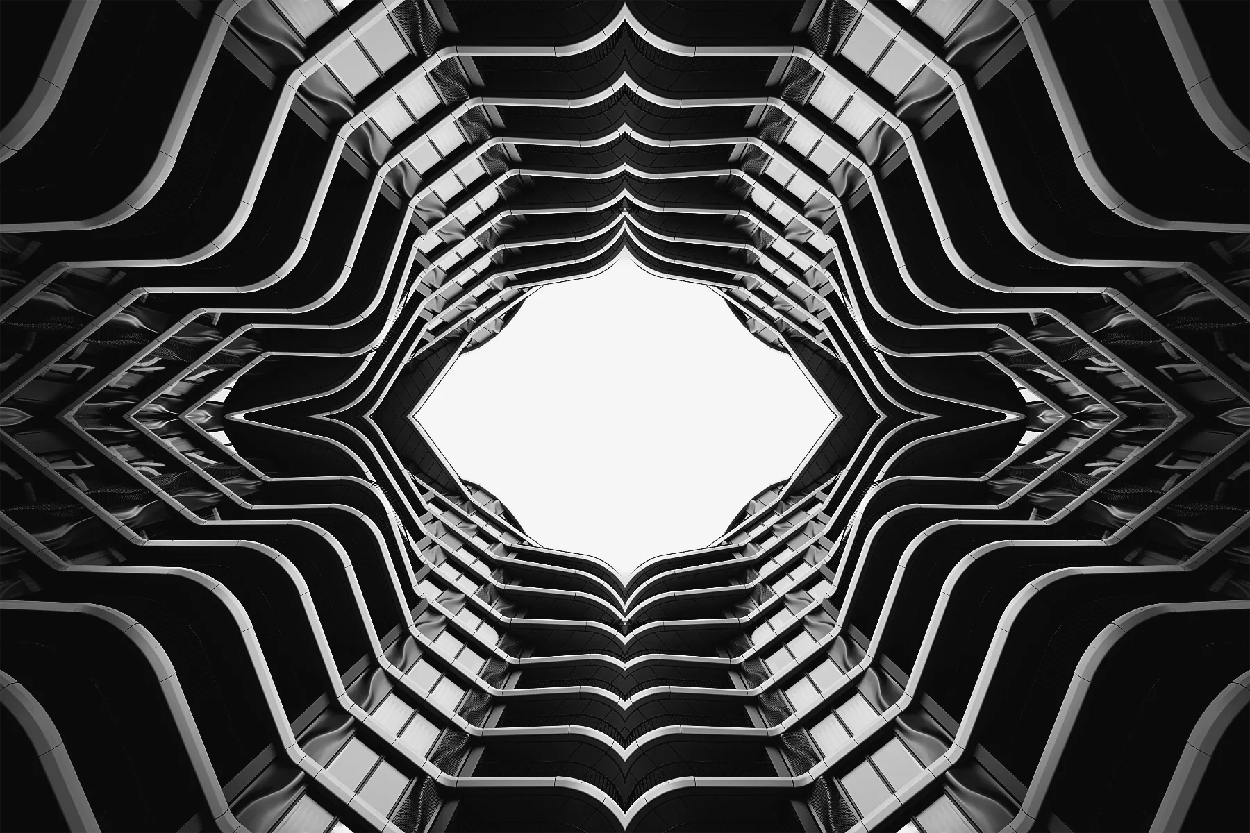 View looking up at the interior of a modern multi-story building with curved balconies forming a hexagonal shape around a central open space, captured in black and white.