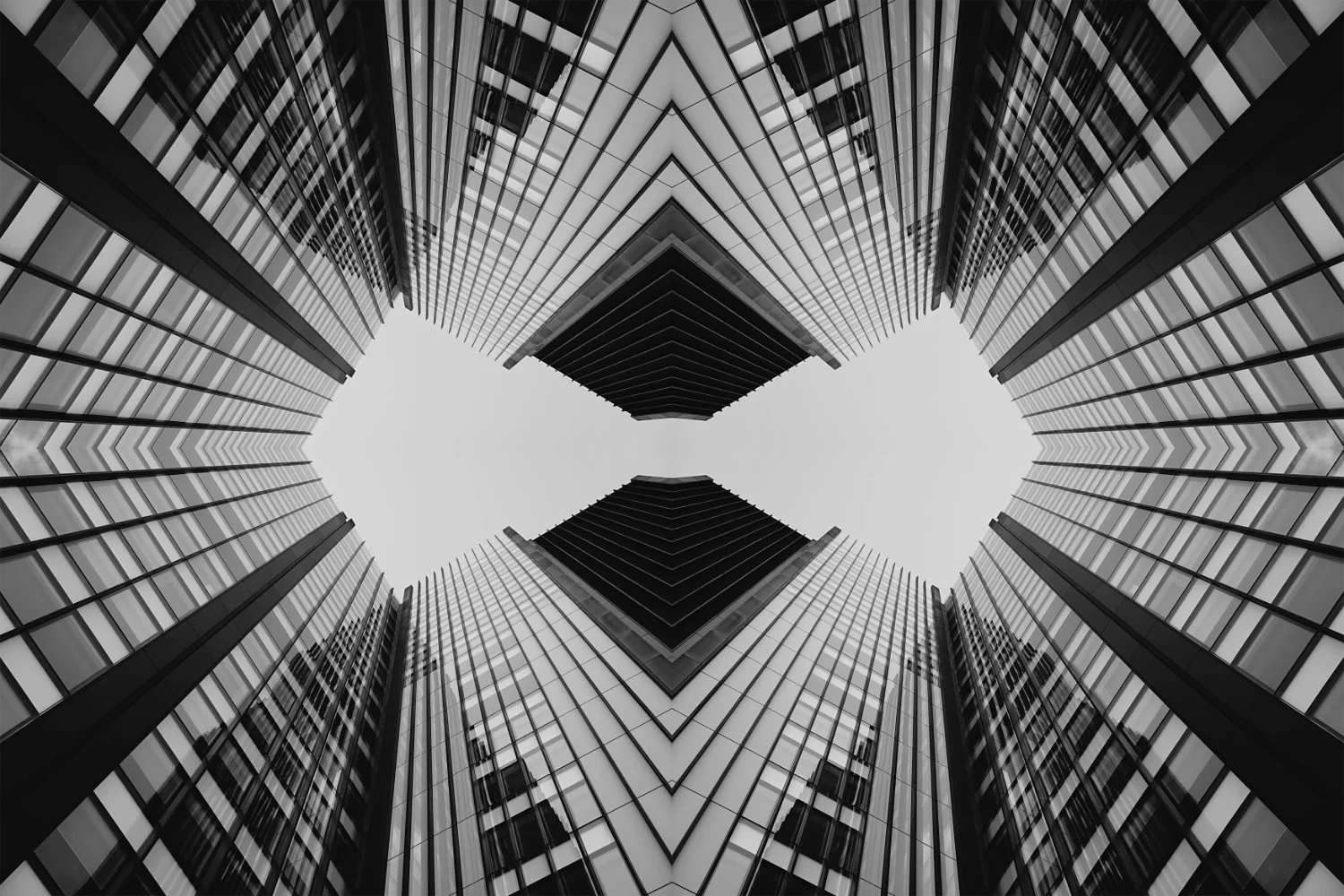 Looking up at tall modern glass skyscrapers converging towards the sky, with a symmetrical pattern.