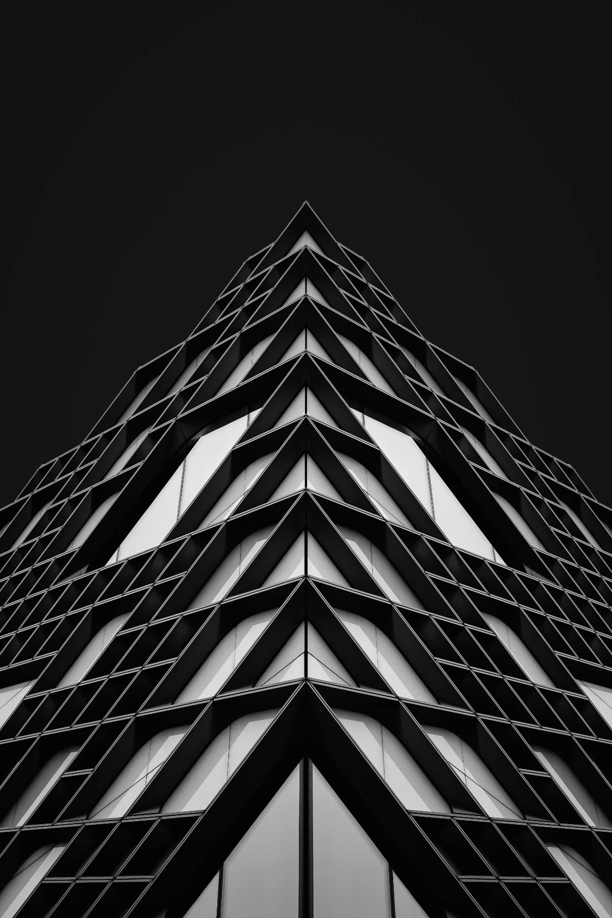 Low-angle black-and-white photo of a modern glass skyscraper with geometric patterns and sharp lines, against a dark sky.