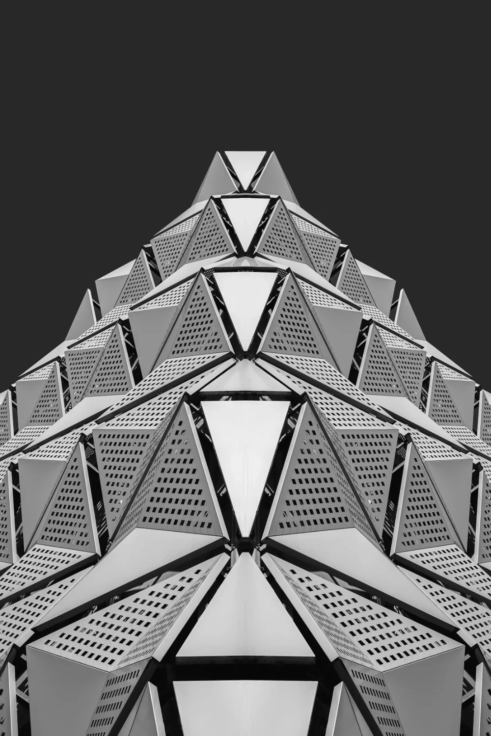 Close-up view of a modern building with geometric, triangular metal panels and perforated surfaces, set against a dark sky.