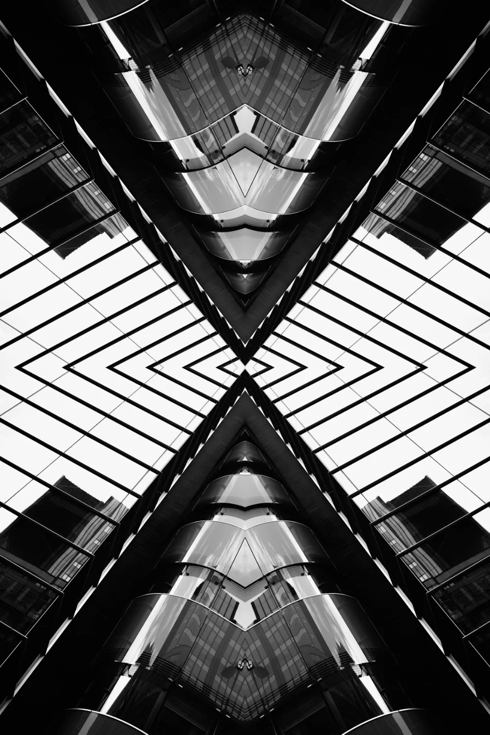 A black and white photo of a modern building with glass windows and reflections, taken from a low angle looking up to create a symmetrical, abstract pattern.