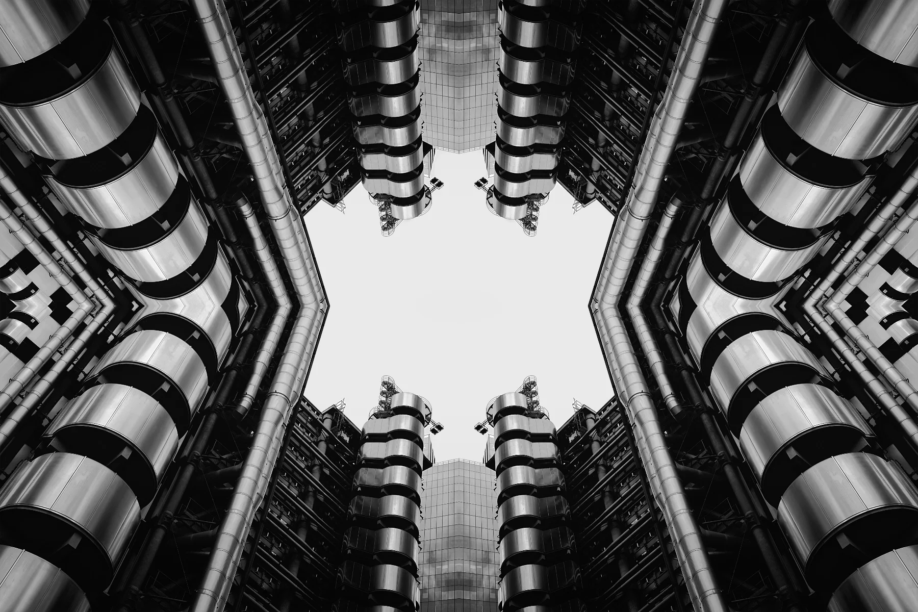 Monochrome view looking up at a modern skyscraper's inner courtyard, featuring symmetrical design, metallic exterior, rounded balconies, and extensive piping and structural elements.