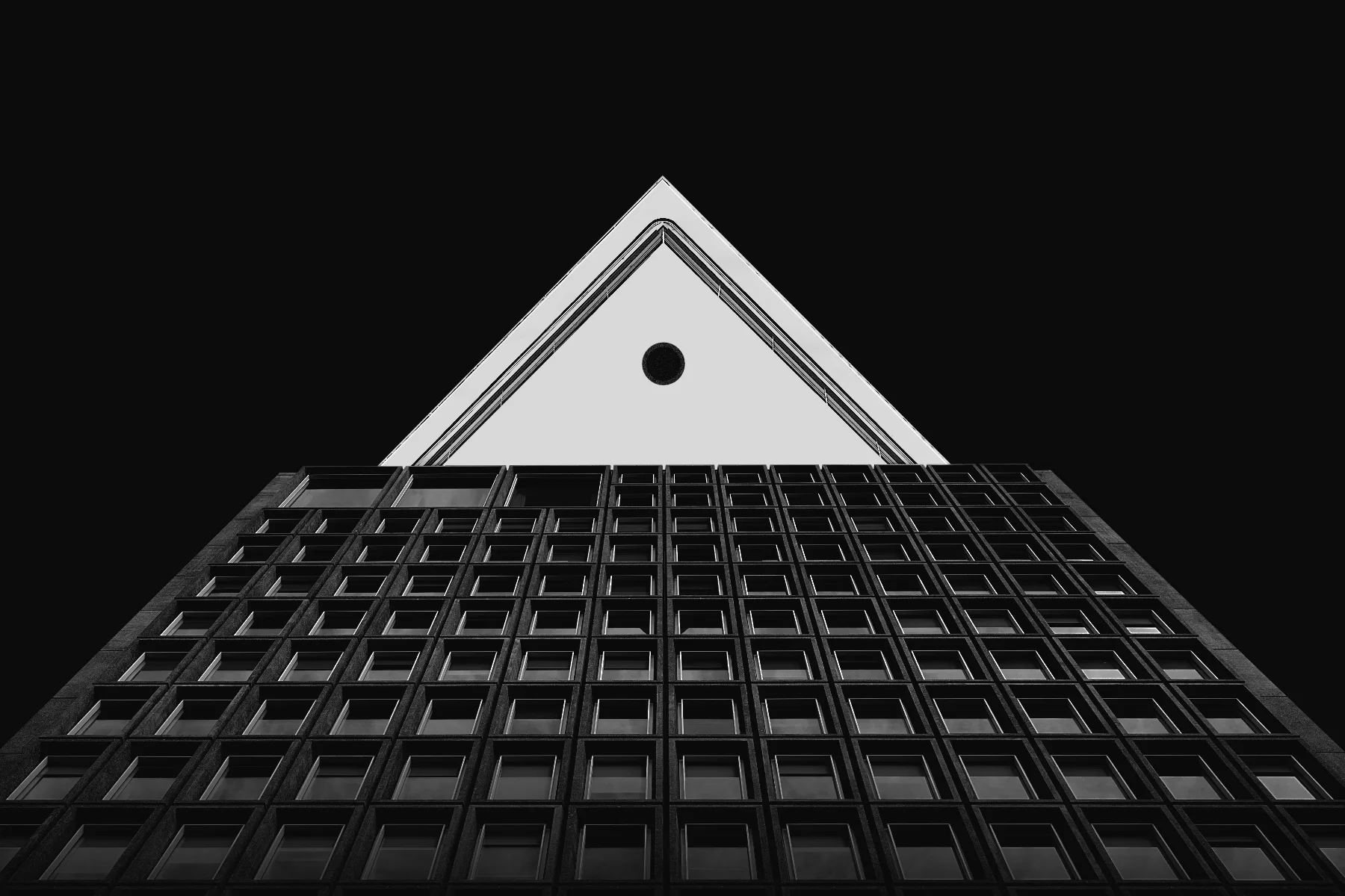 Low-angle black-and-white photo of a modern high-rise building against a black sky, emphasizing the building's geometric pattern of windows and roofline.
