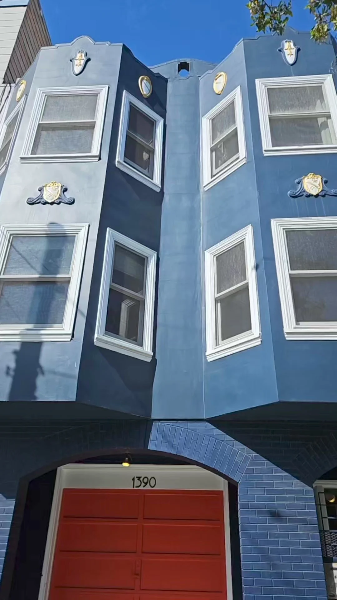 A whimsical blue building with white trim and decorative embellishments, featuring multiple windows and an arched entrance with the number 1390 above the doorway.