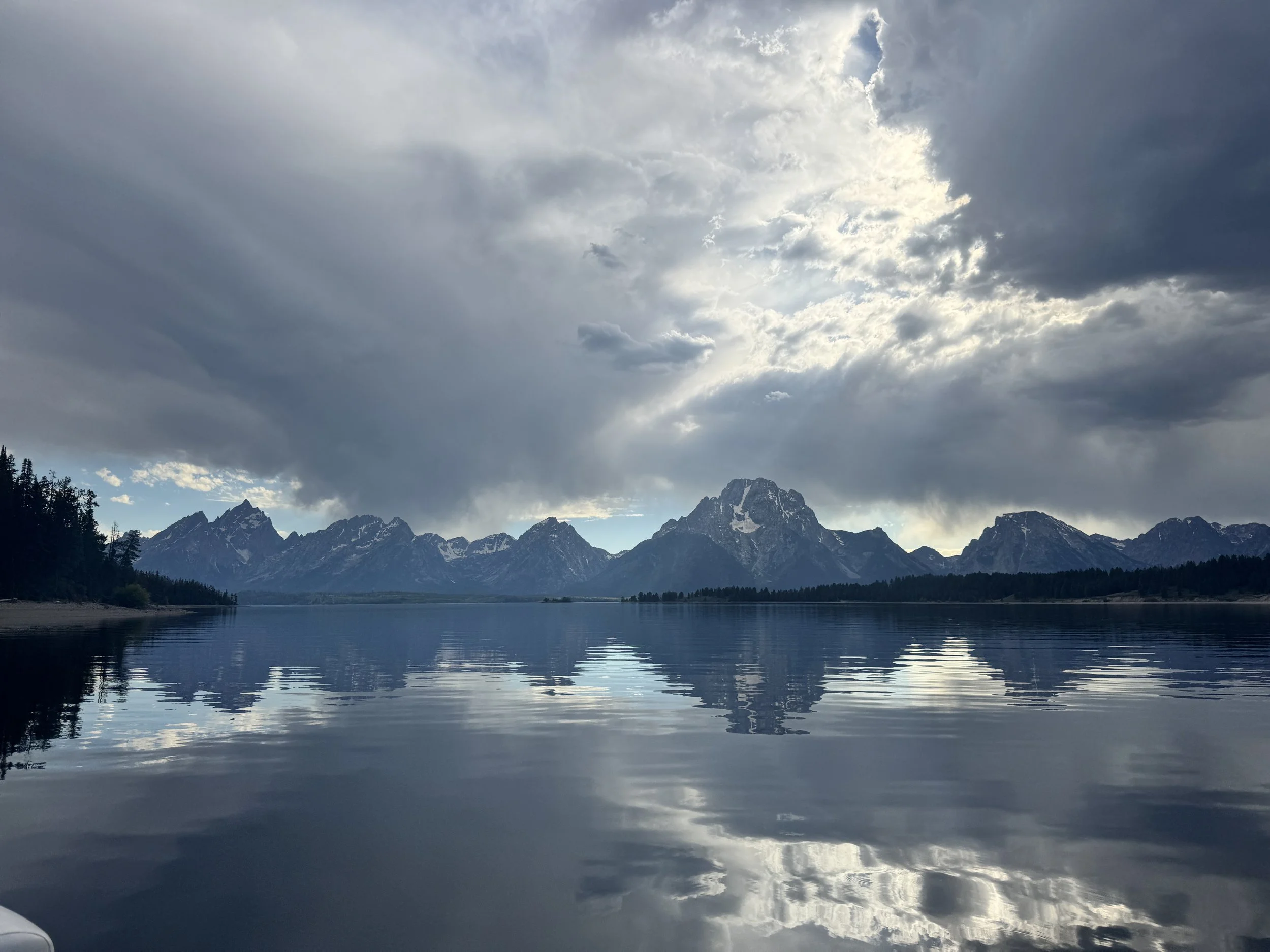 A mountain range with snow-capped peaks reflected in a calm lake under a cloudy sky.