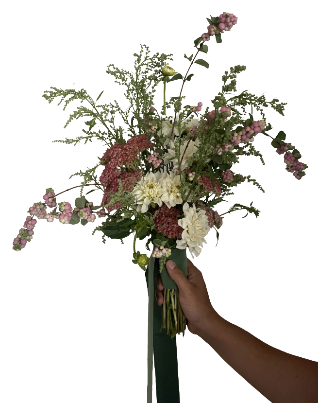 A hand holding a bouquet of assorted flowers with pink and white blooms and green foliage, tied with a green ribbon.