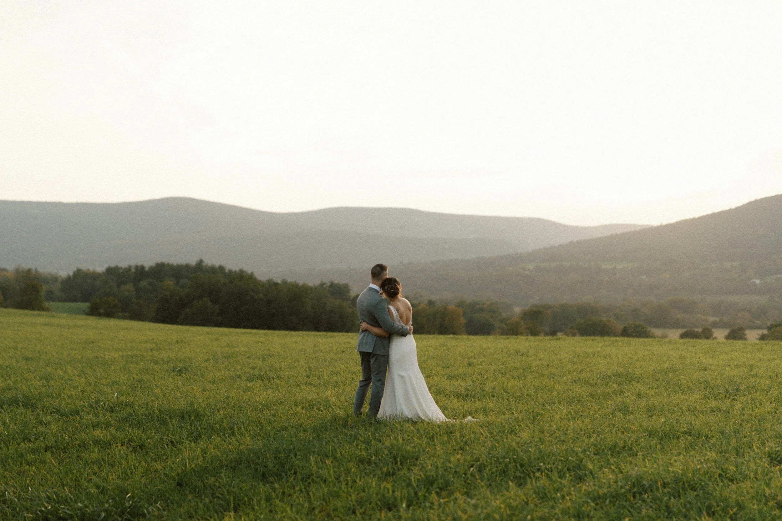 Couple de mariés dans une prairie face aux montagnes au coucher du soleil