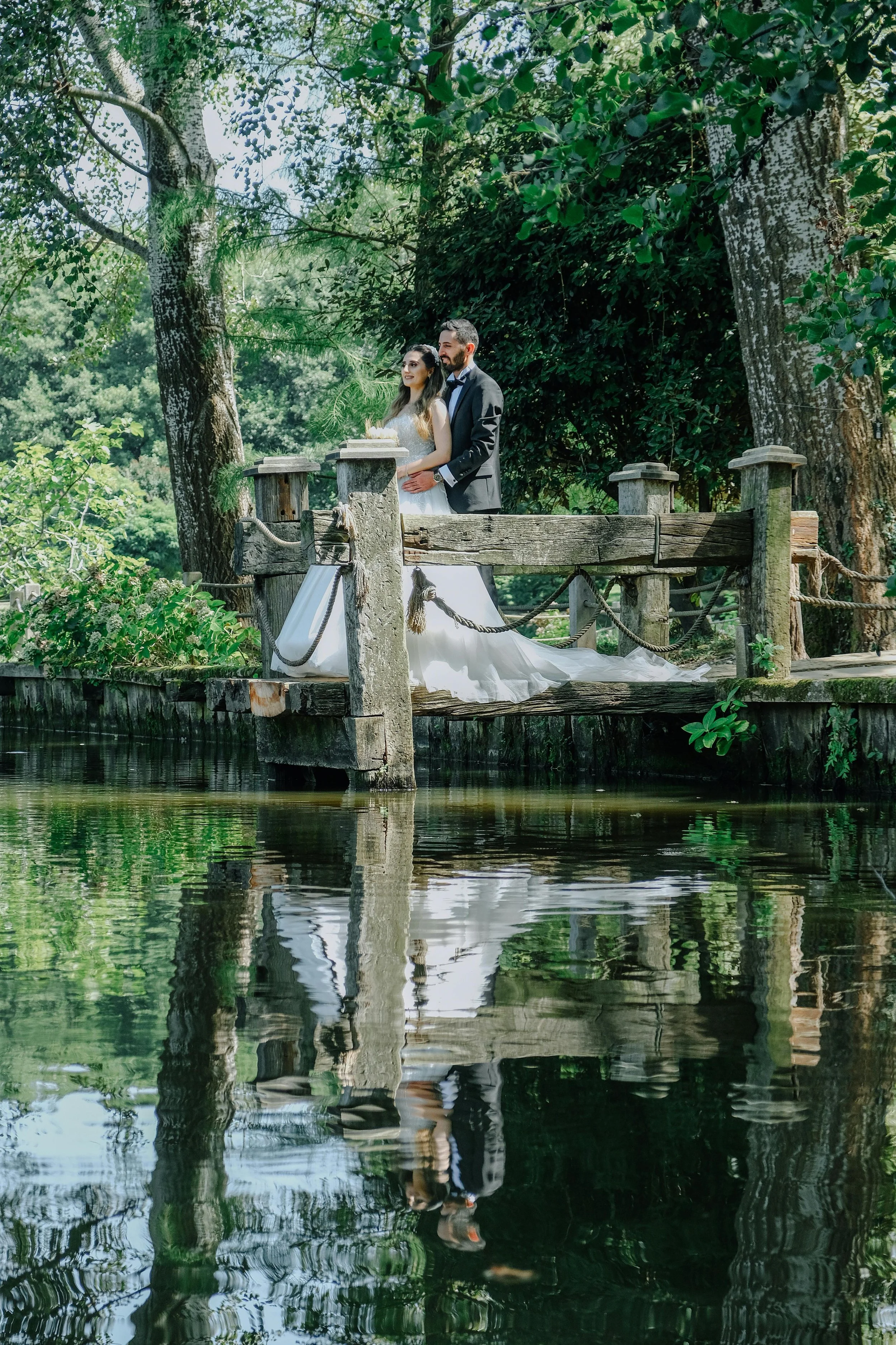 Couple de mariés sur un ponton en bord d'étang, entouré d'arbres