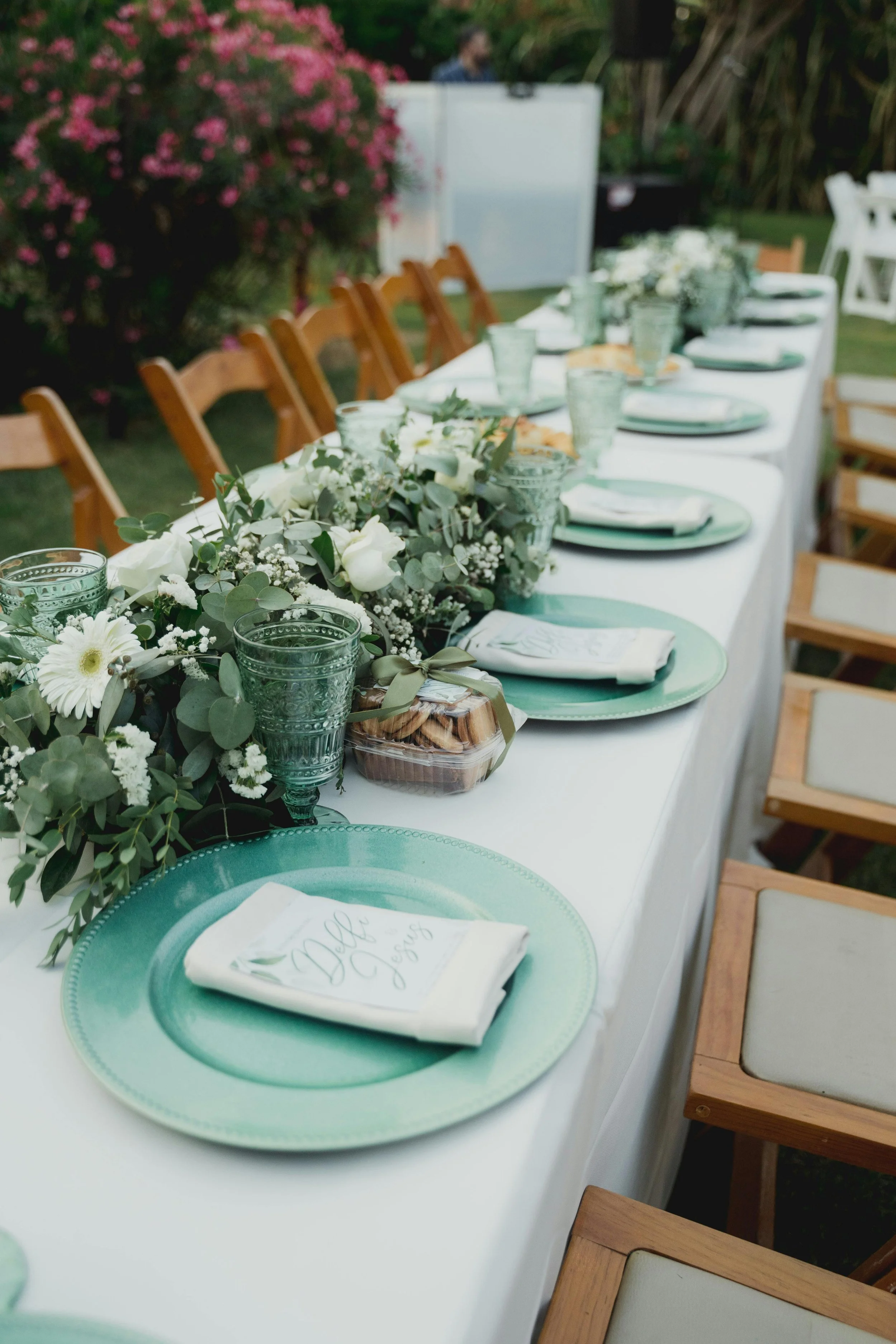 Table de réception de mariage dressée en extérieur avec vaisselle verte et fleurs blanches