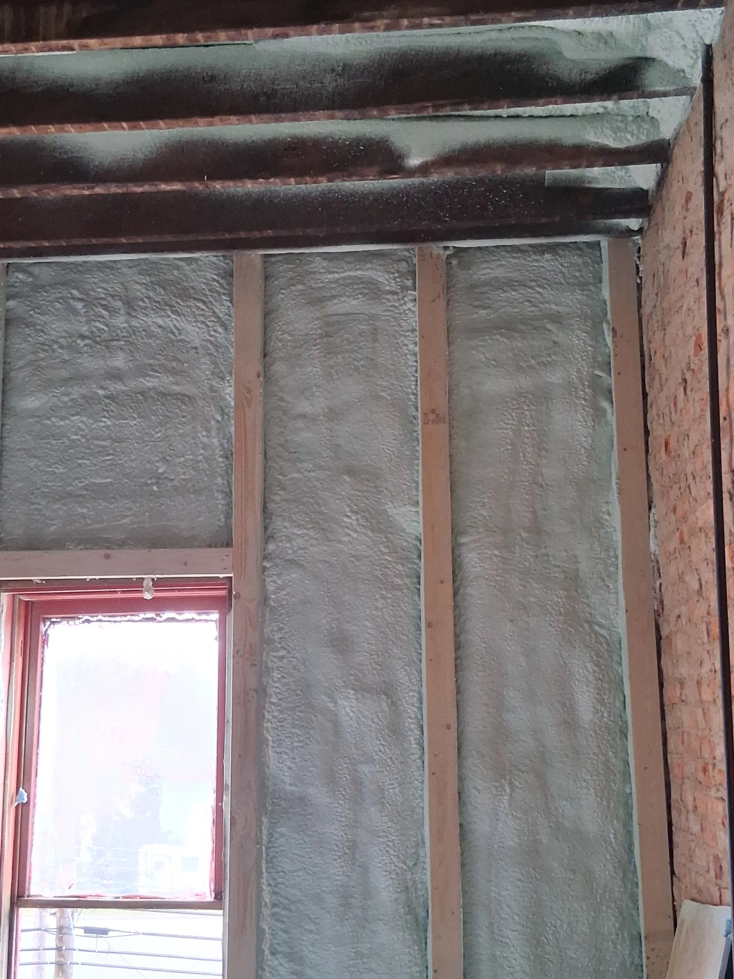 Interior wall with spray foam insulation between wooden studs and a window frame.