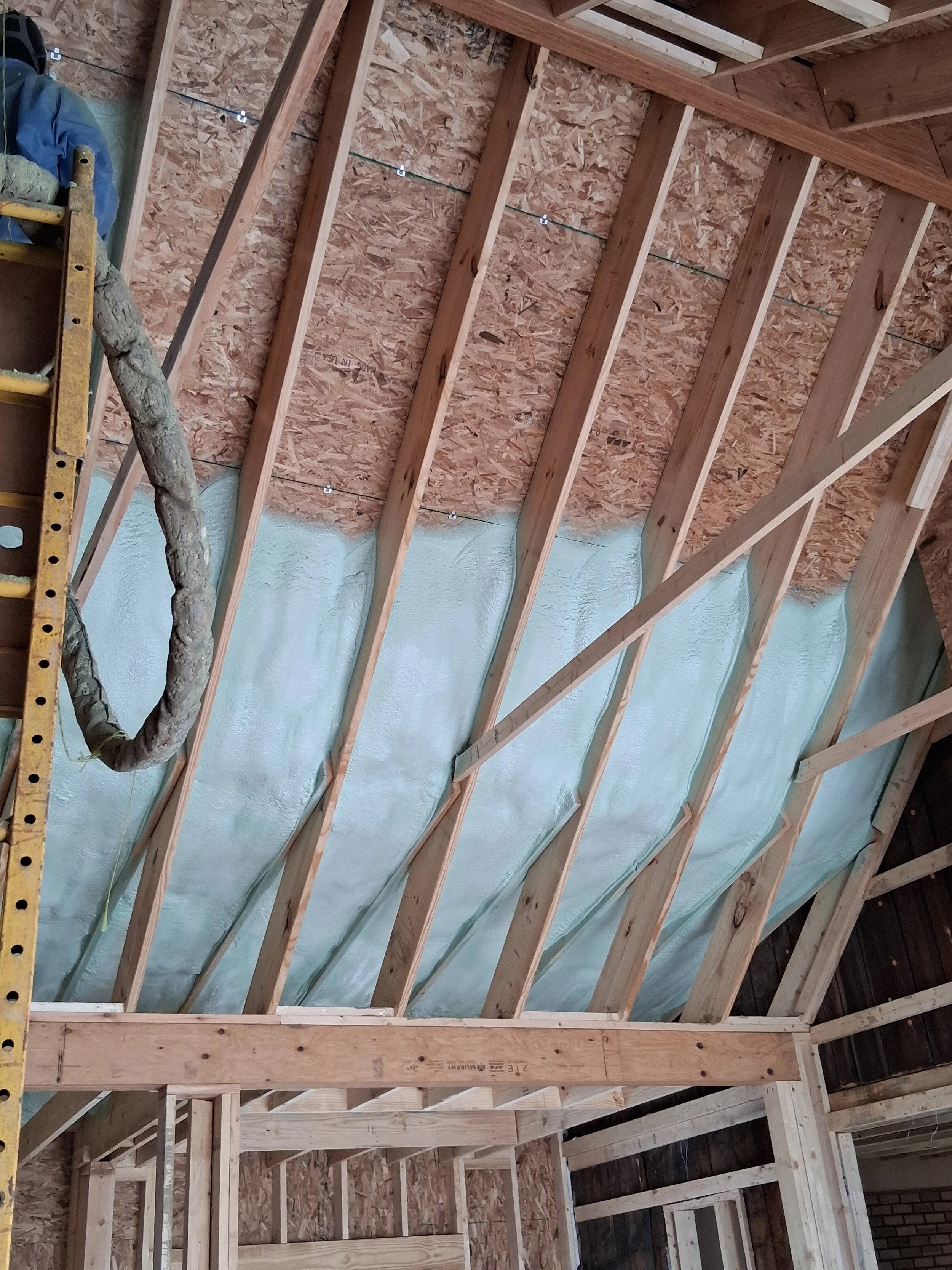Wooden framing of a building interior under construction with insulation being installed on the ceiling.
