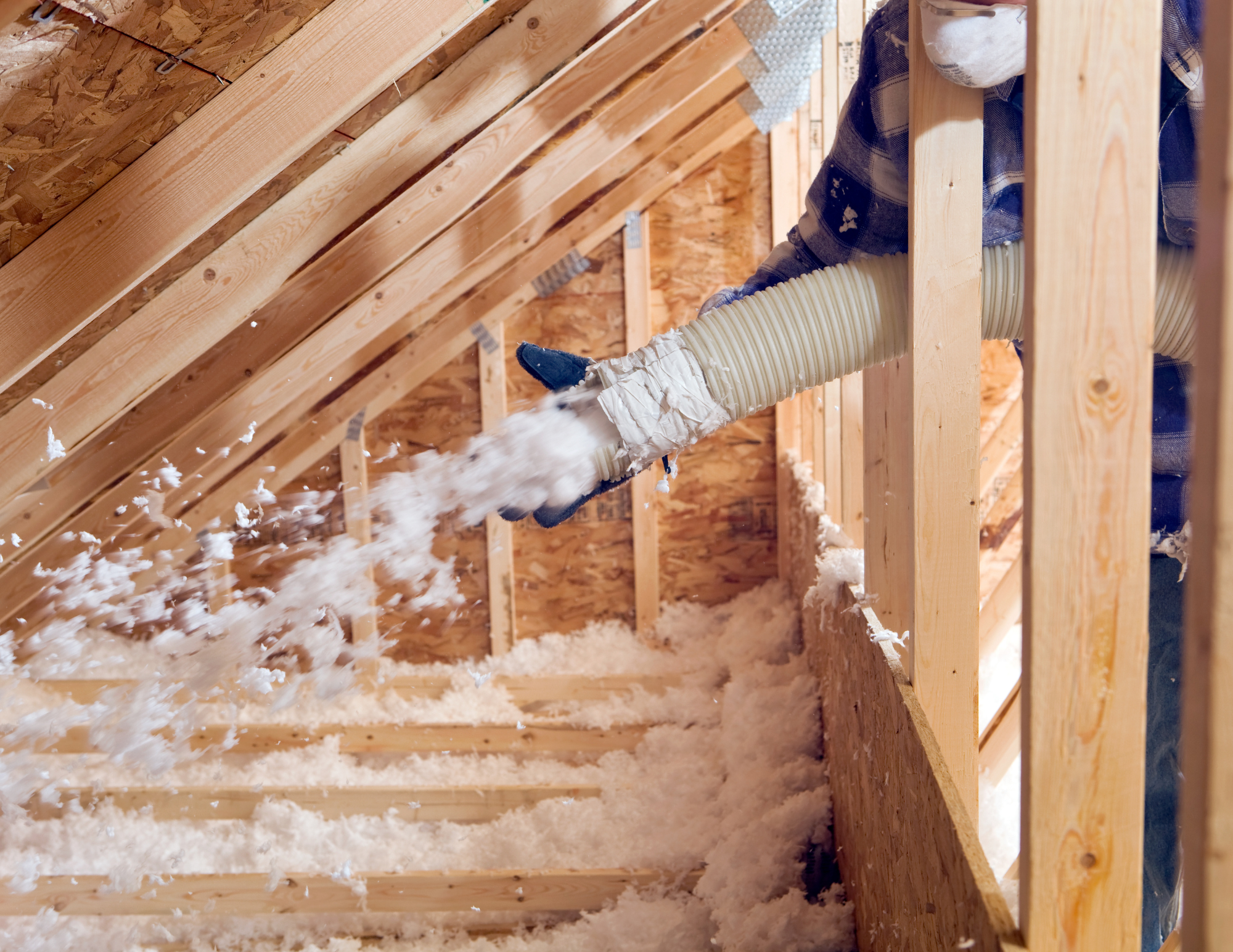 Person using a hose to blow insulation into the attic space through a flexible duct.