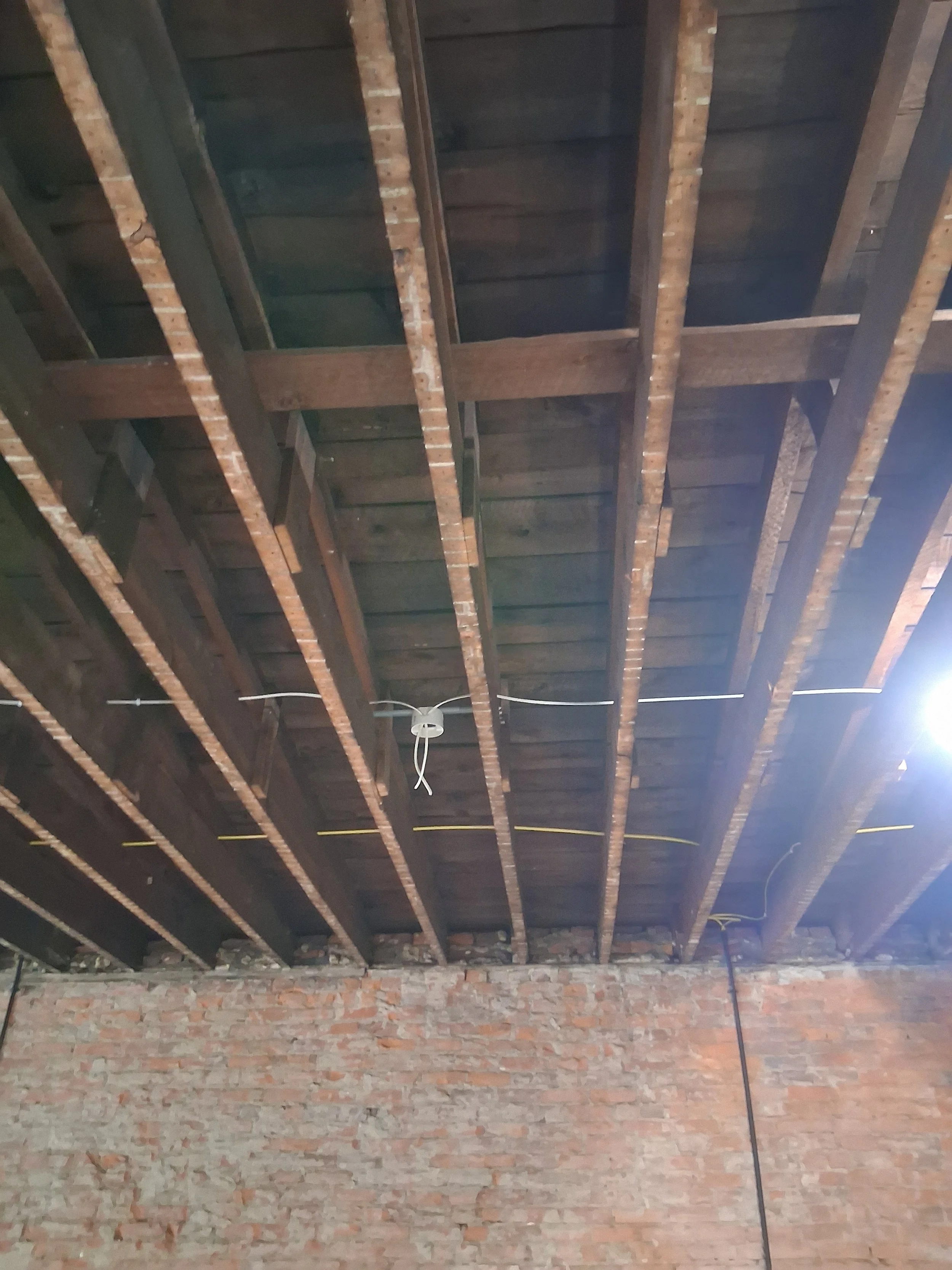 Interior image of a building under construction, showing exposed wooden ceiling beams and brick walls.