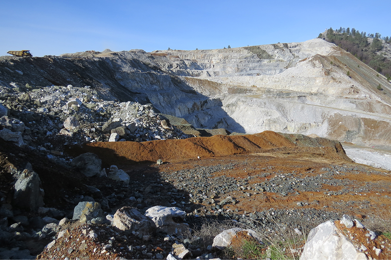 An open-pit mine with terraced layers, rocky debris, and a mining truck in view.