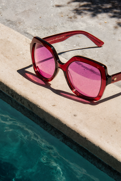 Pink sunglasses resting on a concrete edge beside a swimming pool