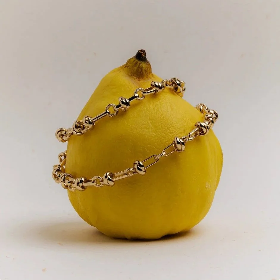 A yellow lemon with a silver beaded necklace draped around it, against a plain background.