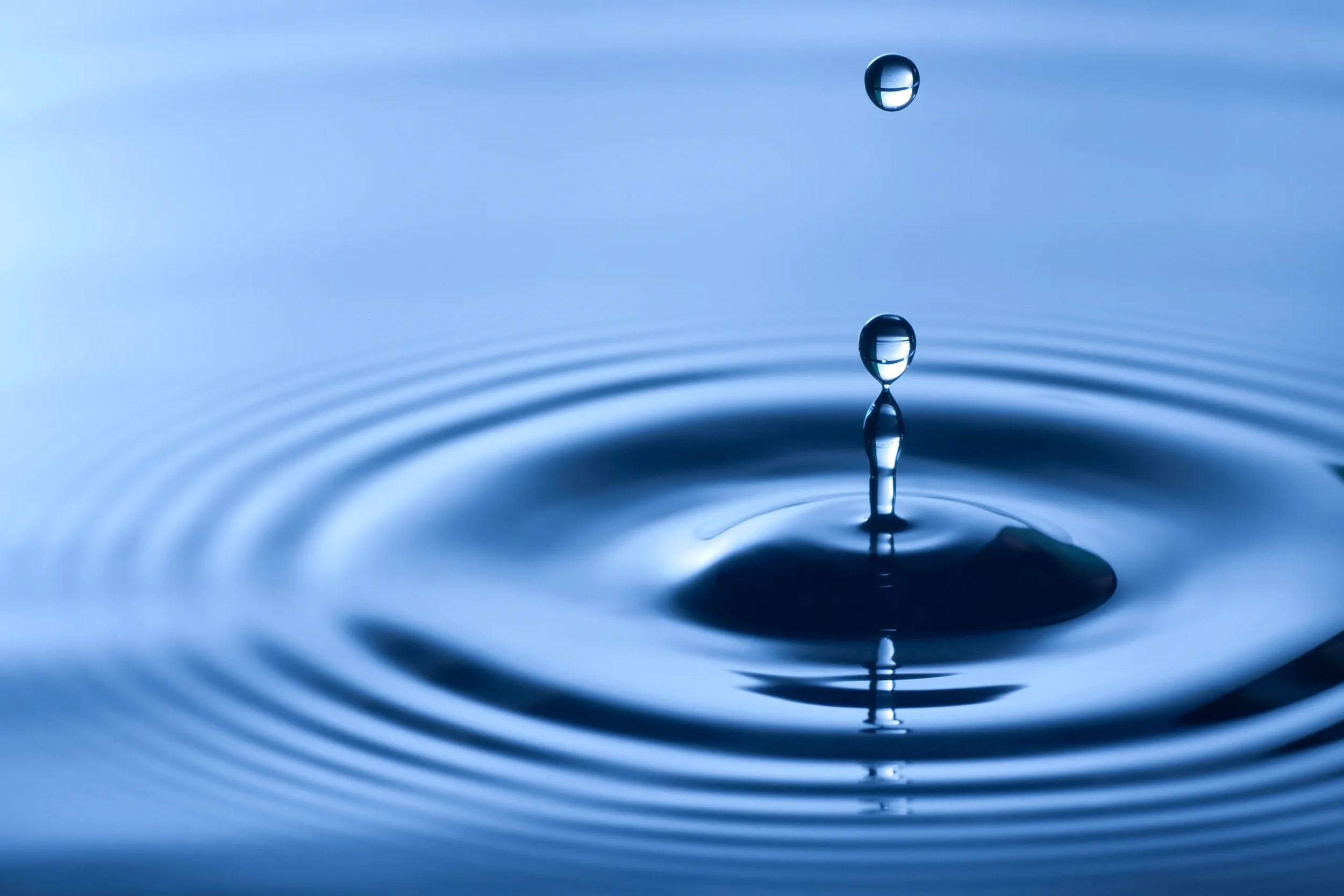 Close-up photo of a water droplet creating ripples on the surface of water.