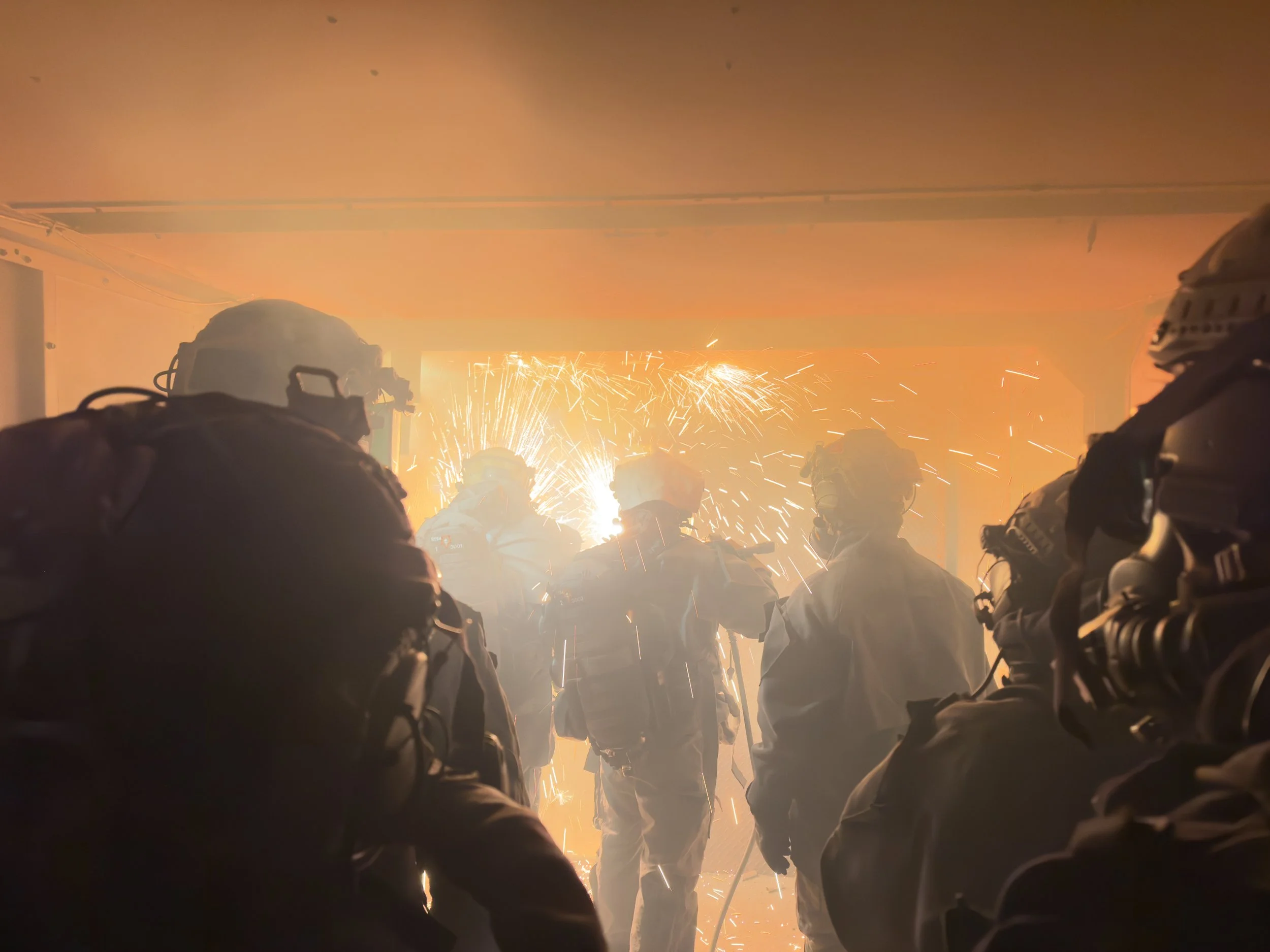 Firefighters entering a smoke-filled room with sparks flying in the background.
