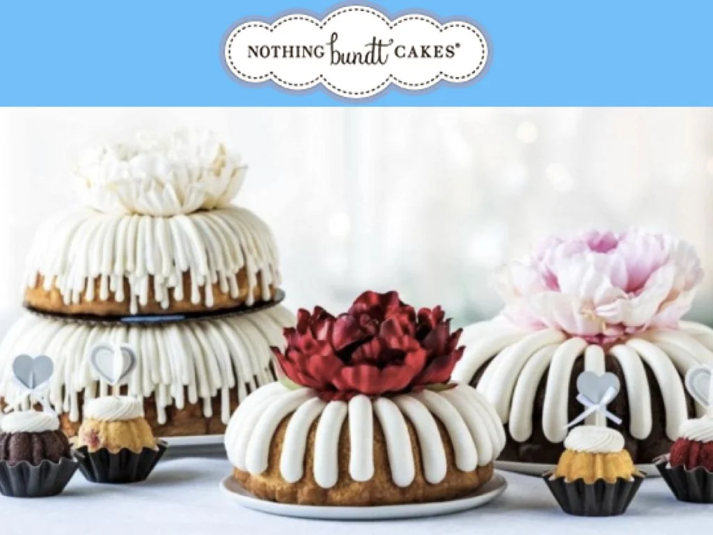 Decorative cakes and cupcakes, some with floral and heart-shaped toppers, displayed on a table for a celebration.