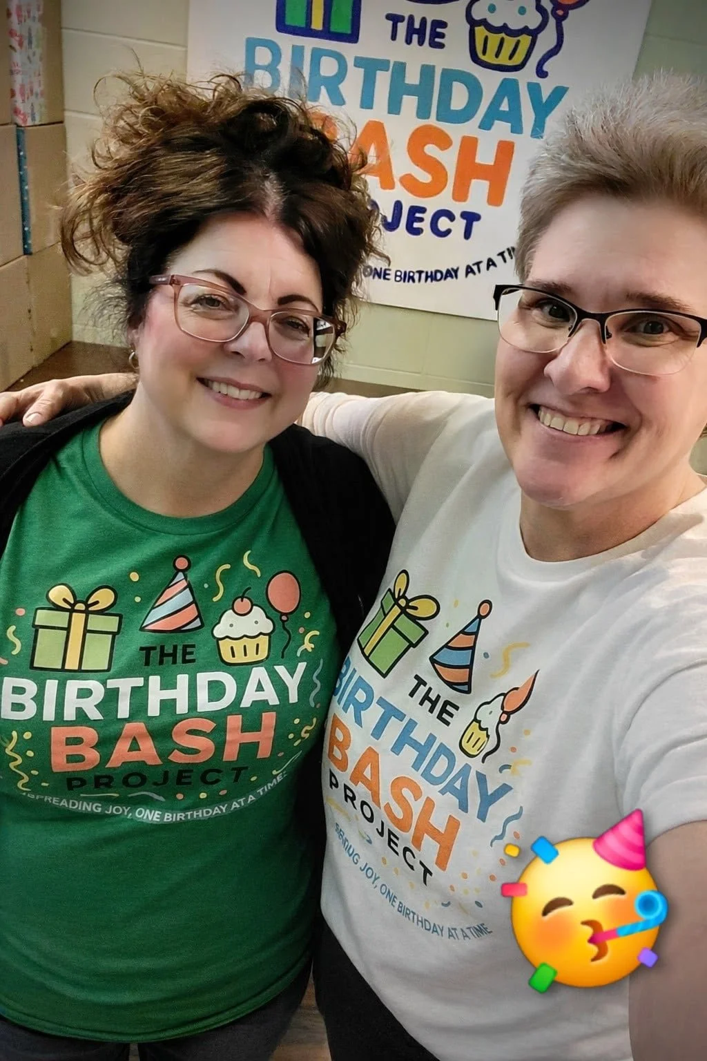 Two people smiling at the camera, wearing T-shirts with colorful birthday-themed graphics and text that reads 'The Birthday Bash Project'. They are at a birthday celebration with a decorated banner in the background that says 'The Birthday Bash Proje