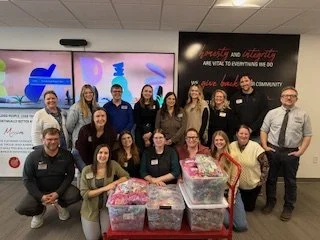 Group of people gathered around tables with packed plastic bags, inside a room with educational posters and screens on the wall.