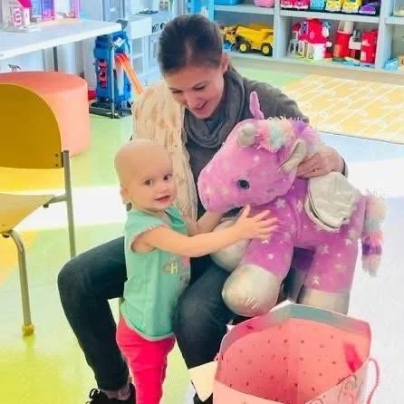 A woman and a young girl playing with a large pink plush unicorn toy in a toy store.