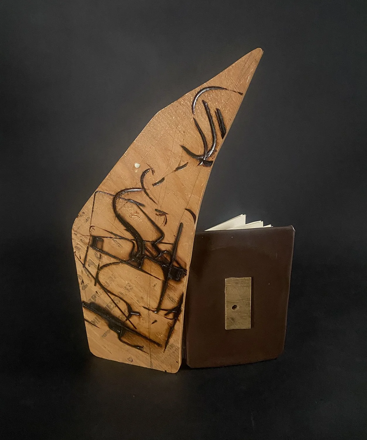 An open book, facing away, with a wooden cover on one side featuring branding burns, the other side covered in brown vinyl, set against a black background.
