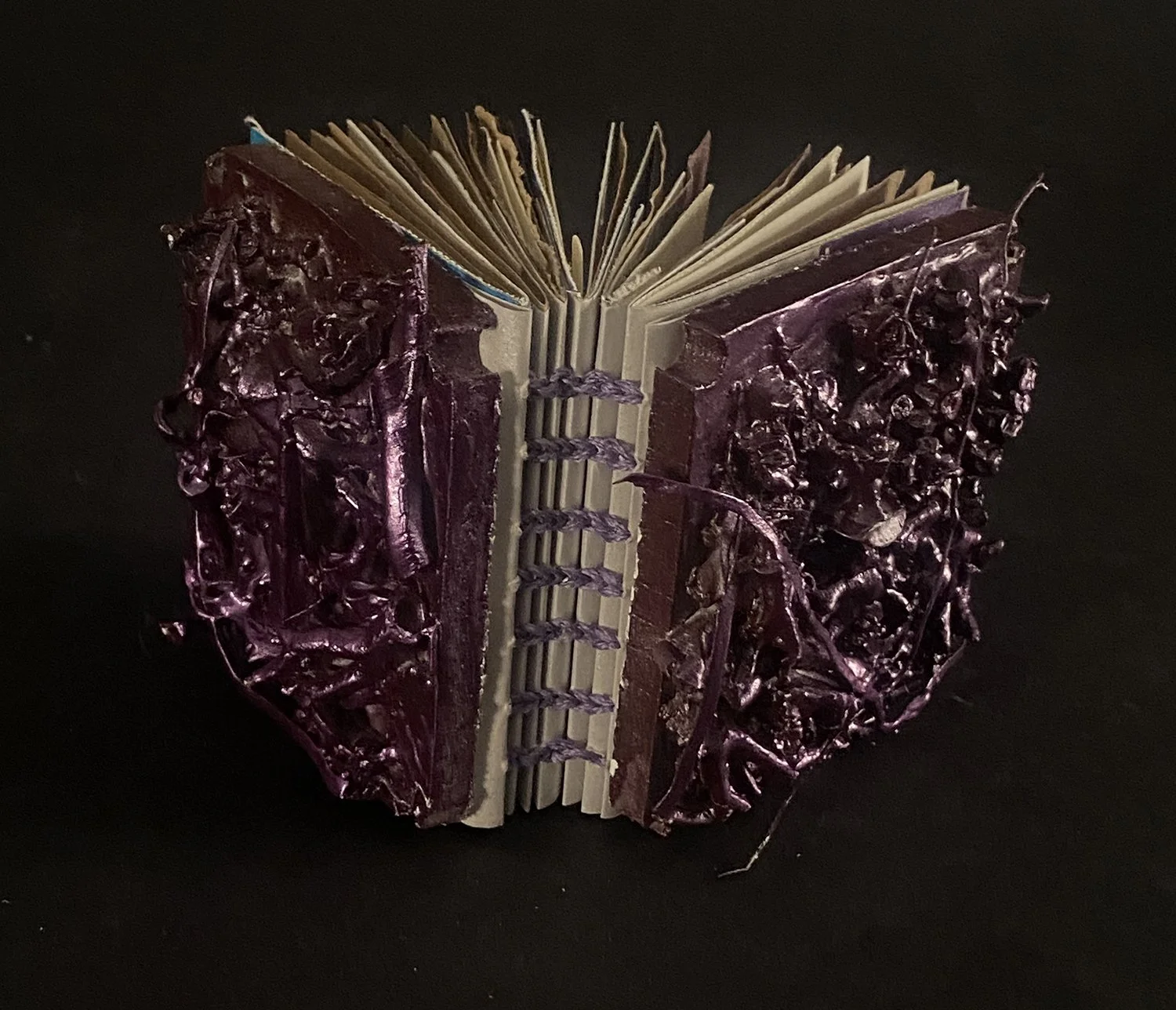A book with dark purple, textured, and glossy pages, open but facing away, with a black background.