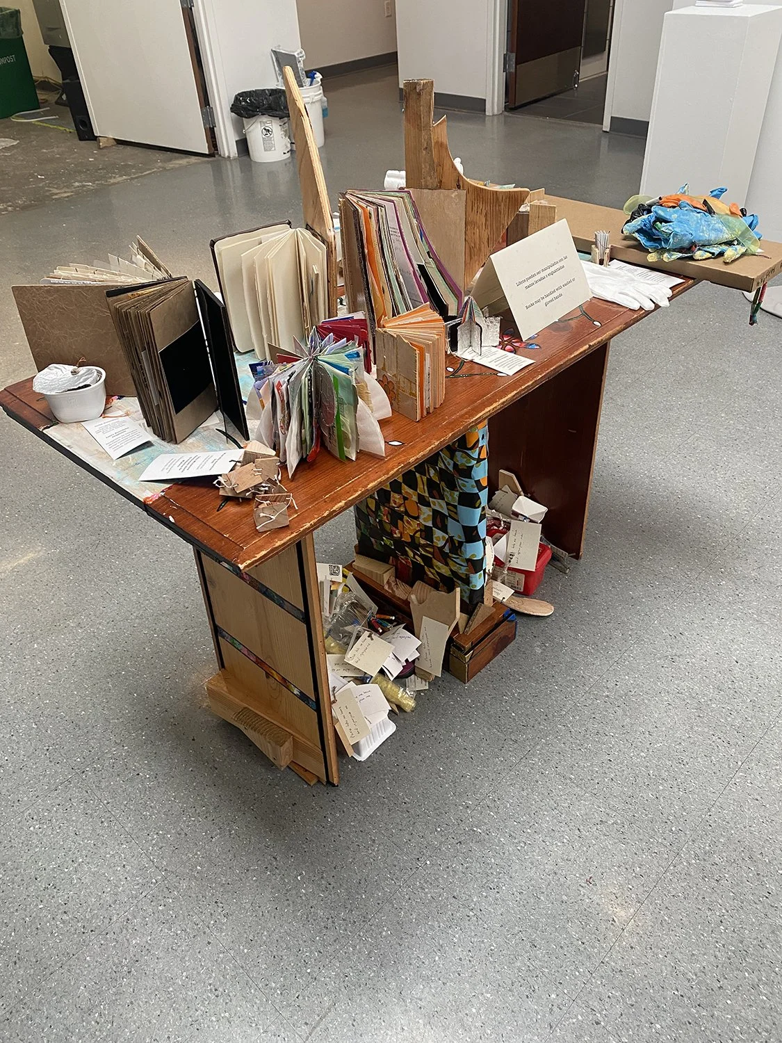 A wooden table displaying a variety of artist books, in a gallery.