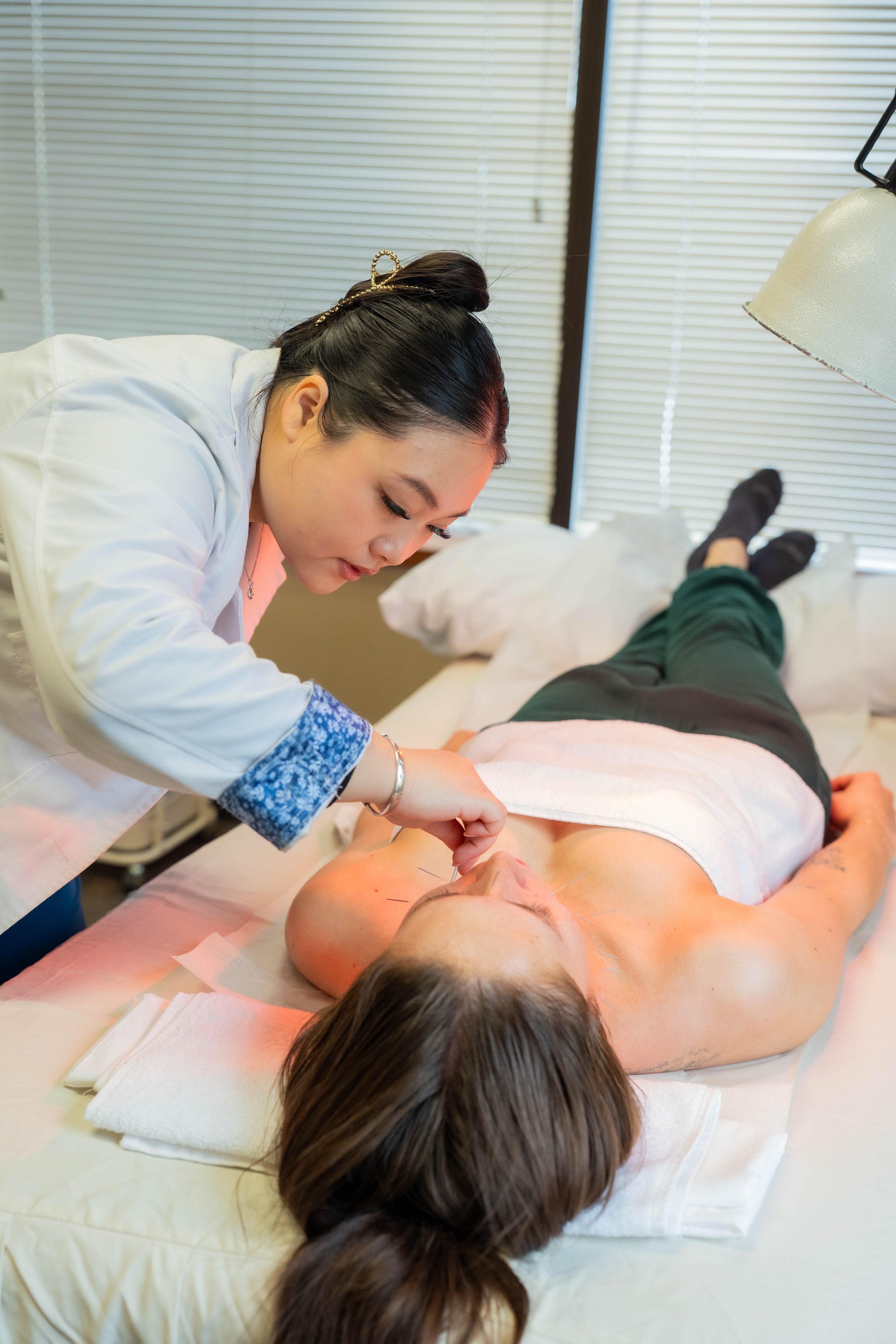 Acupuncturist performing facial acupuncture treatment on a patient lying on a treatment bed in a wellness clinic.