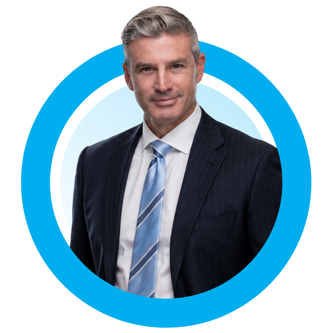 A middle-aged man with grey hair in a dark pinstripe suit, white shirt, and blue striped tie, standing against a blue background with colorful abstract shapes.
