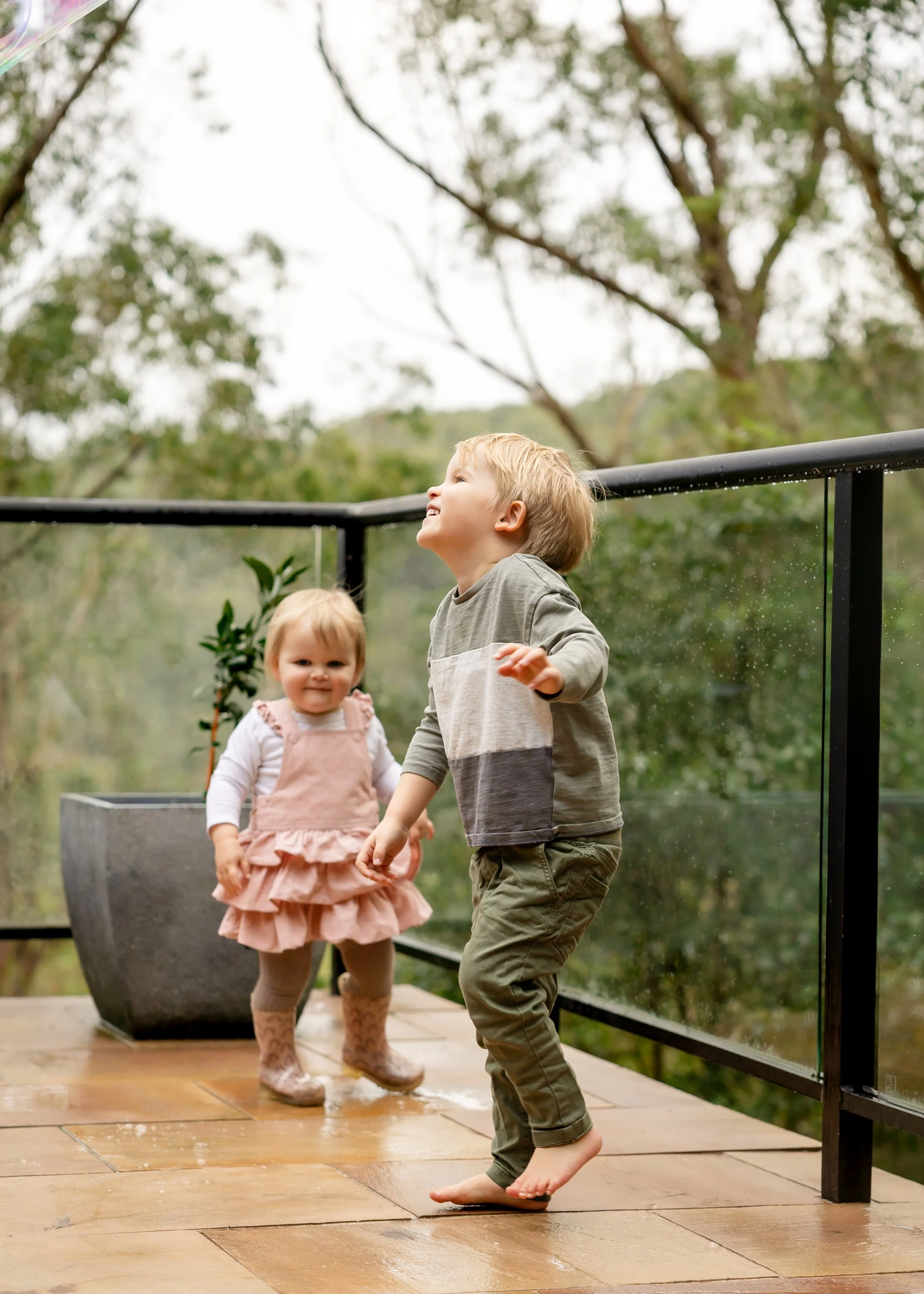 Two young siblings playing on a rainy deck during an in-home family photography session in Sydney