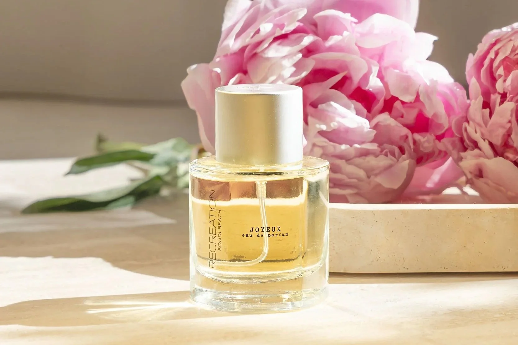 Editorial product photography of perfume bottle styled with pink flowers in soft natural light