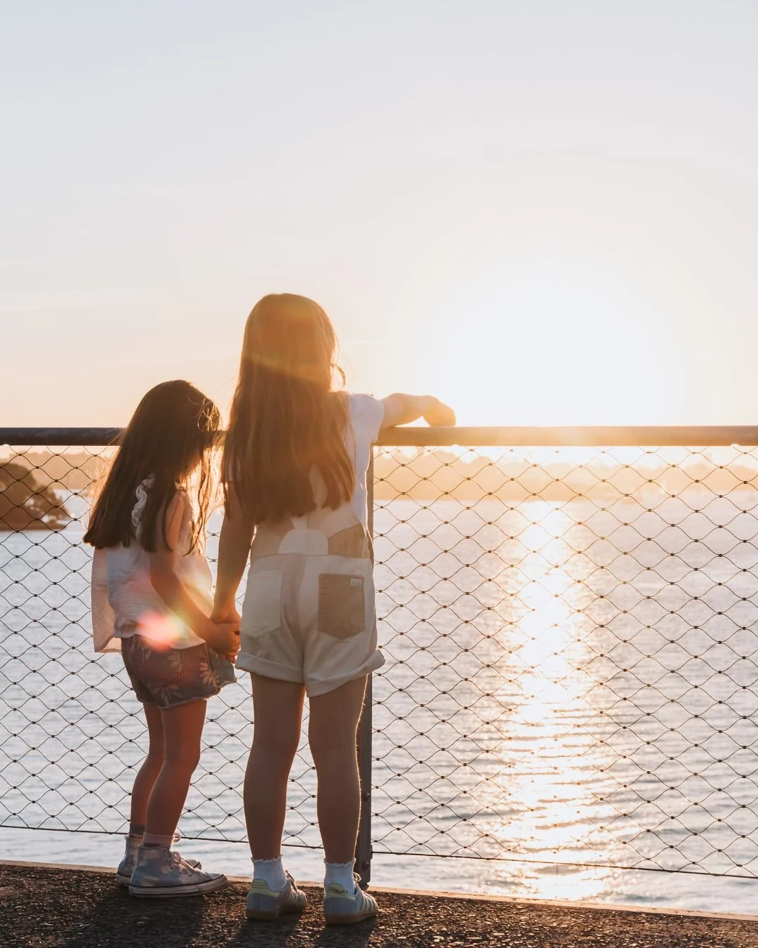 Family photography session in Sydney at sunset capturing two sisters by the water in natural light