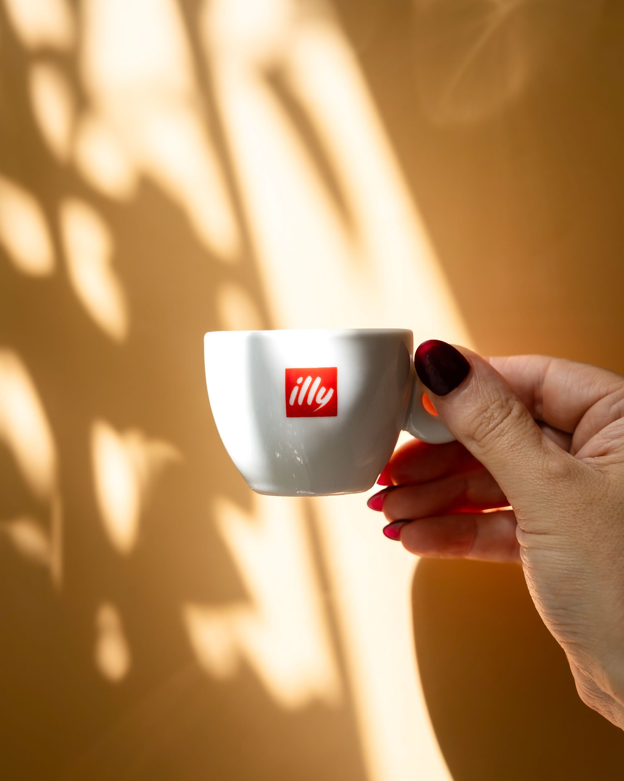Product photography of Illy coffee cup held in hand with warm light and shadow patterns