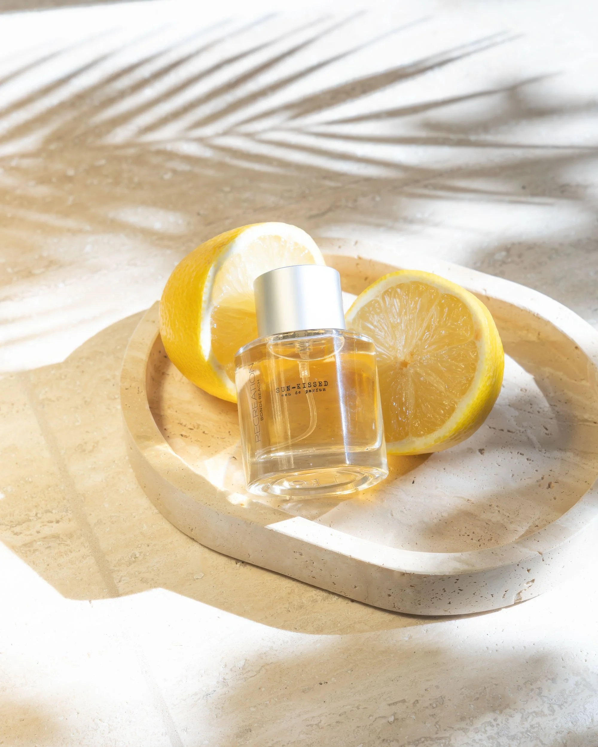Editorial product photography of perfume bottle styled with lemon and natural light shadows