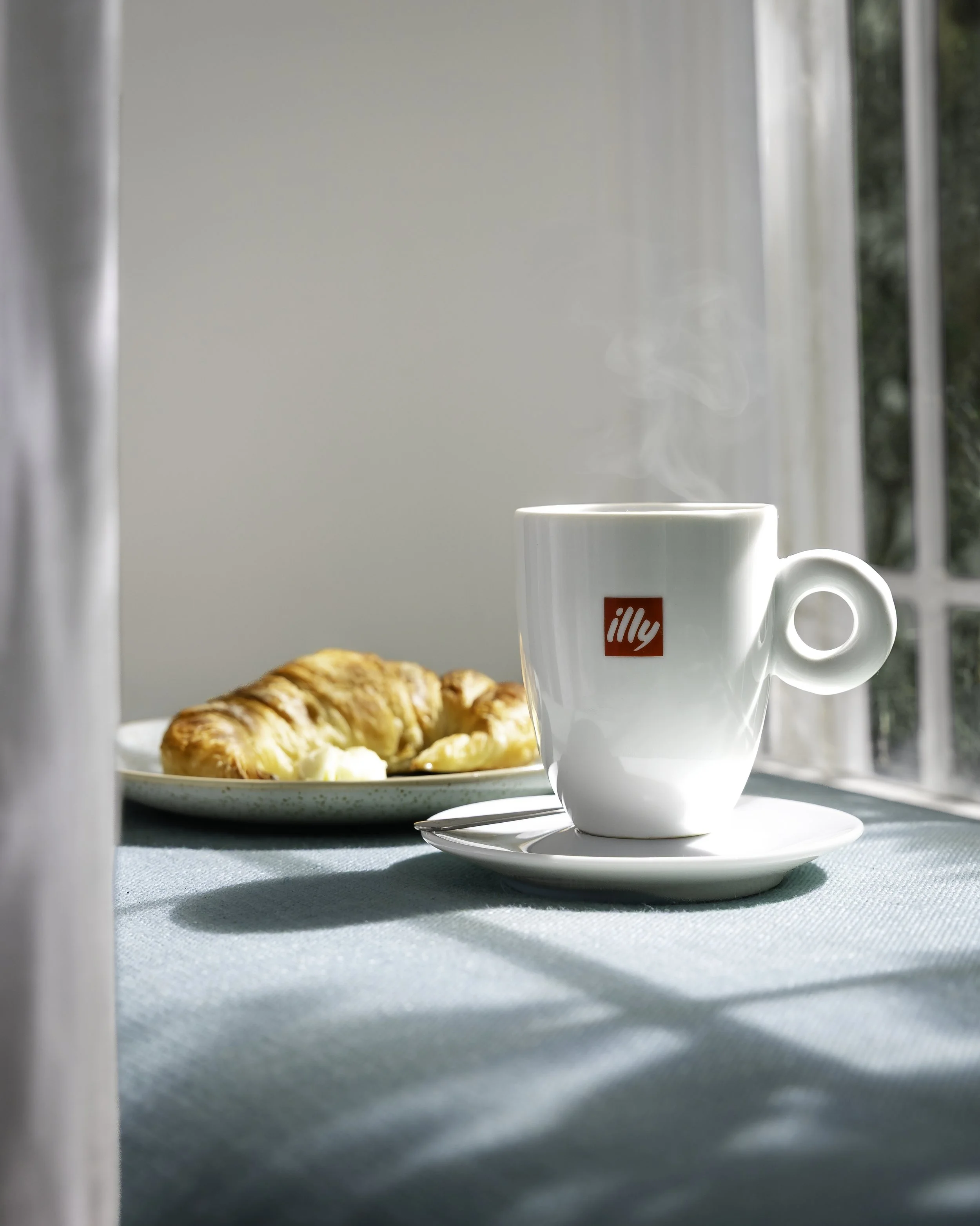 Lifestyle coffee photography featuring Illy cup and croissant in soft natural light