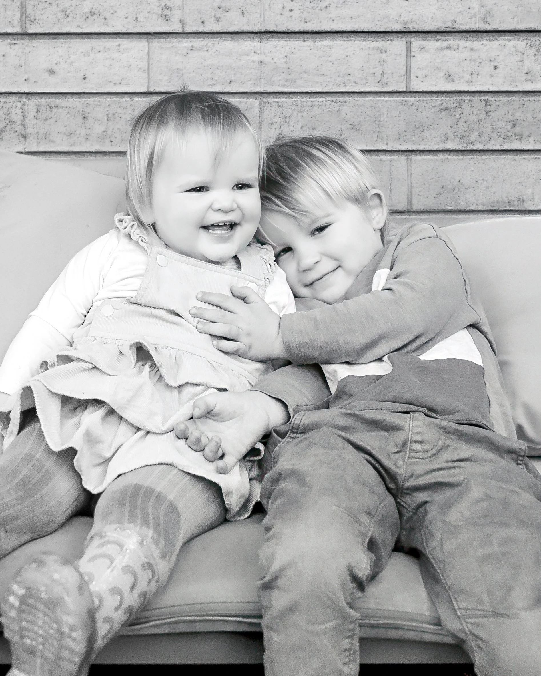 Black and white portrait of two young siblings holding hands against a brick wall - candid family photography by Georgie Meadows, Sydney