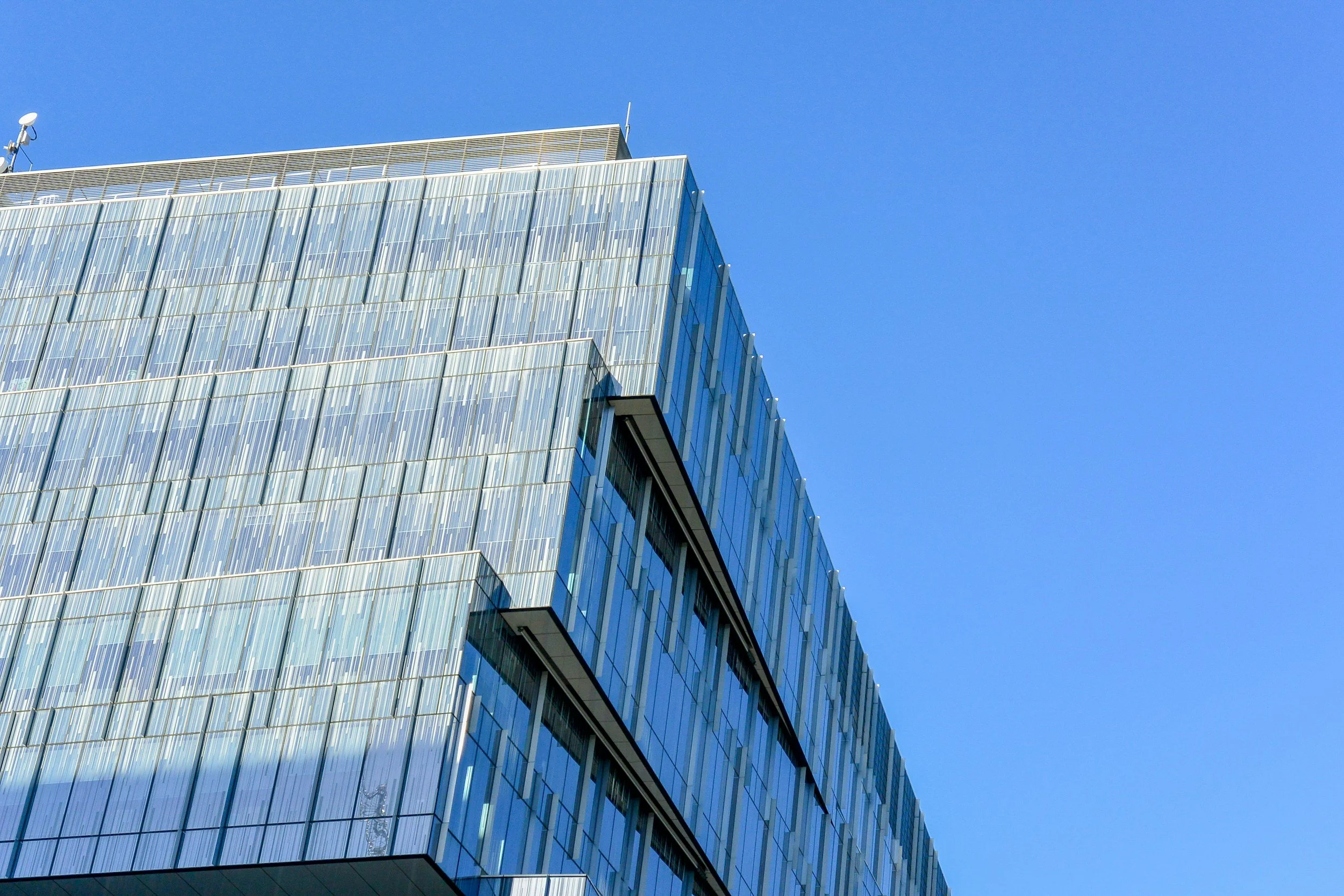 Modern glass office building with reflective windows against a clear blue sky.