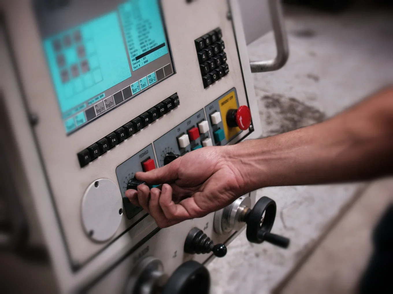 A person's hand adjusting a control knob on an industrial machine panel with a digital display and various buttons.
