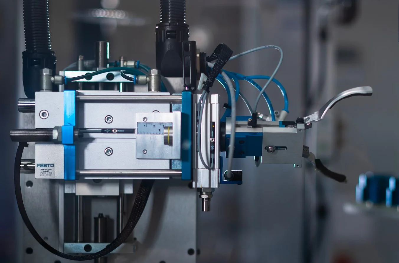 Close-up of a mechanical device or machine with metal components, tubes, and wires, likely used in industrial or laboratory settings.
