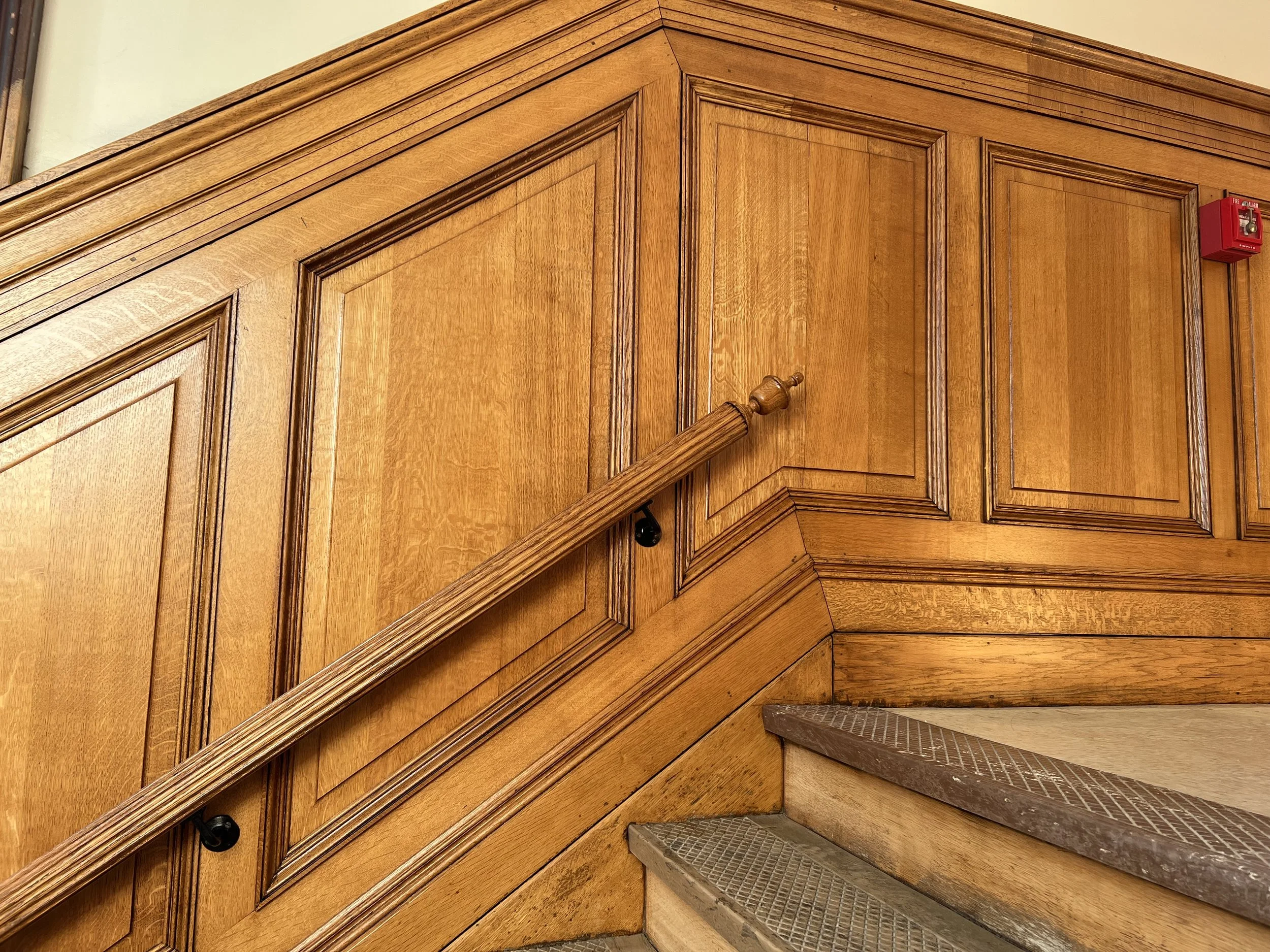 Wood-paneled staircase corner with railing and a fire alarm nearby.