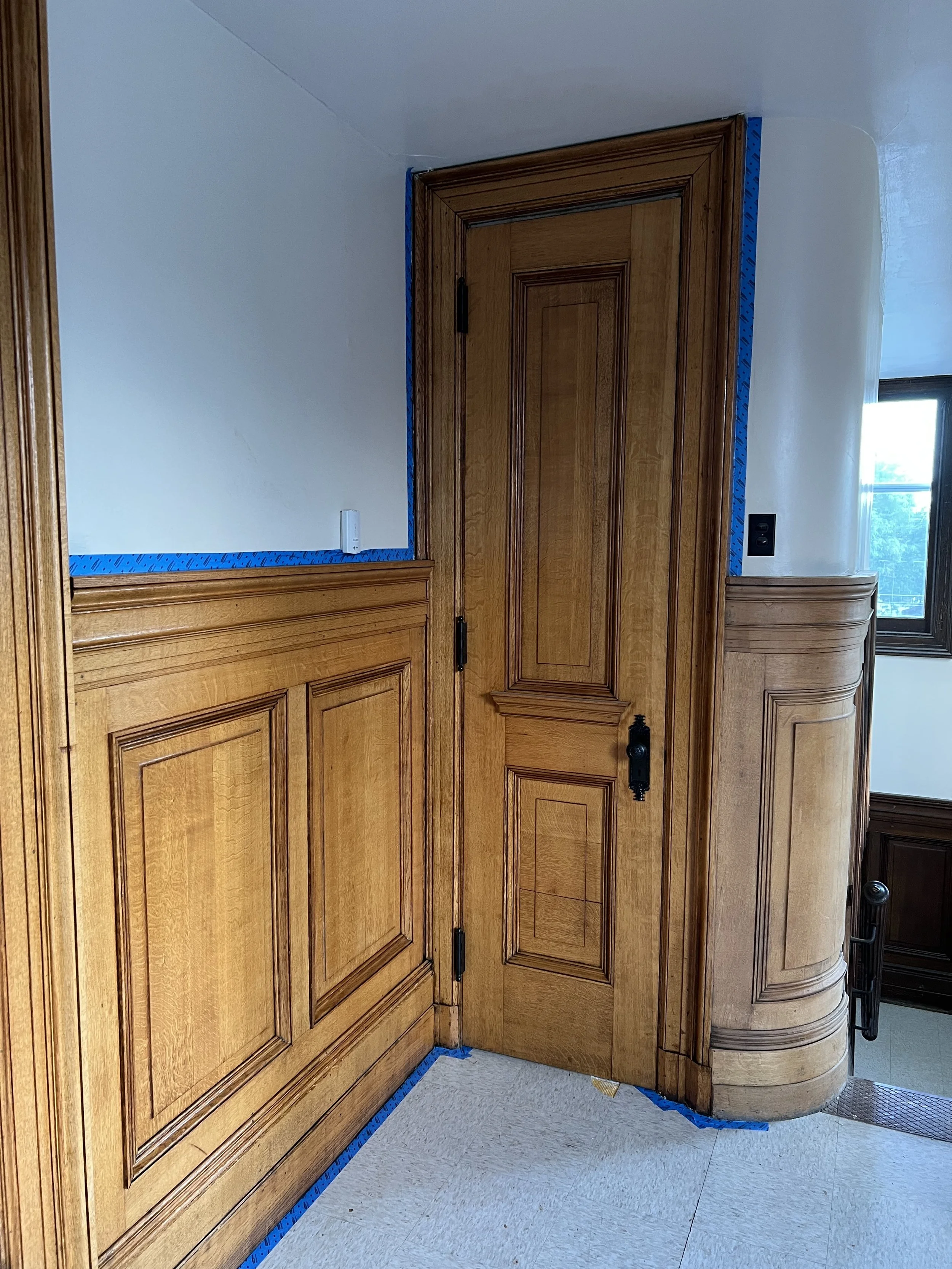Wooden kitchen cabinets with blue painter's tape along edges, partially open door, and visible floor.