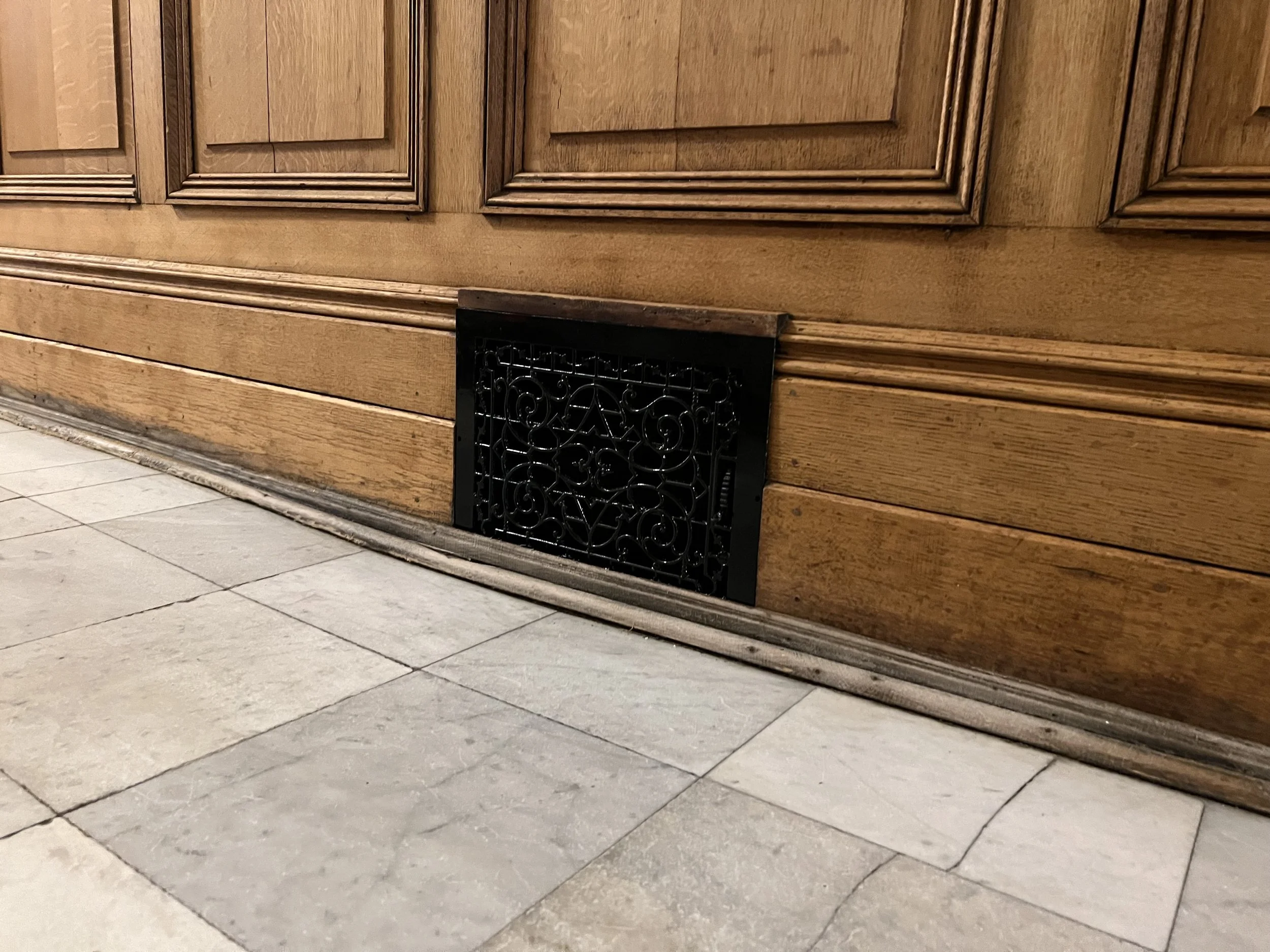 Close-up of a floor register with crown molding details and a black decorative vent below, set on a tiled floor.